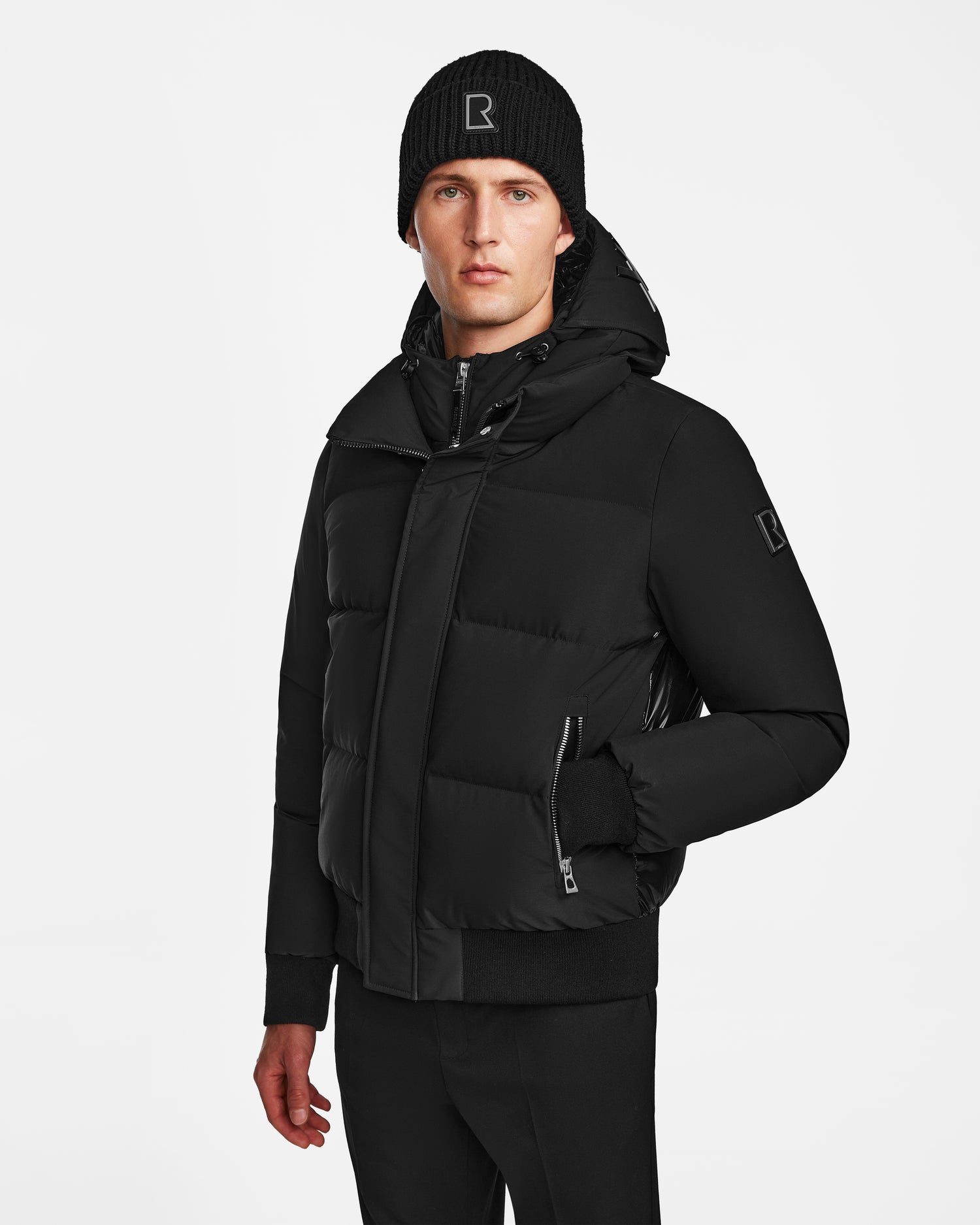 A man wears the Rudsak JORDY - 9123513 Black M recycled stormshell puffer jacket, paired with a black beanie and pants, standing against a plain white background with a neutral expression.