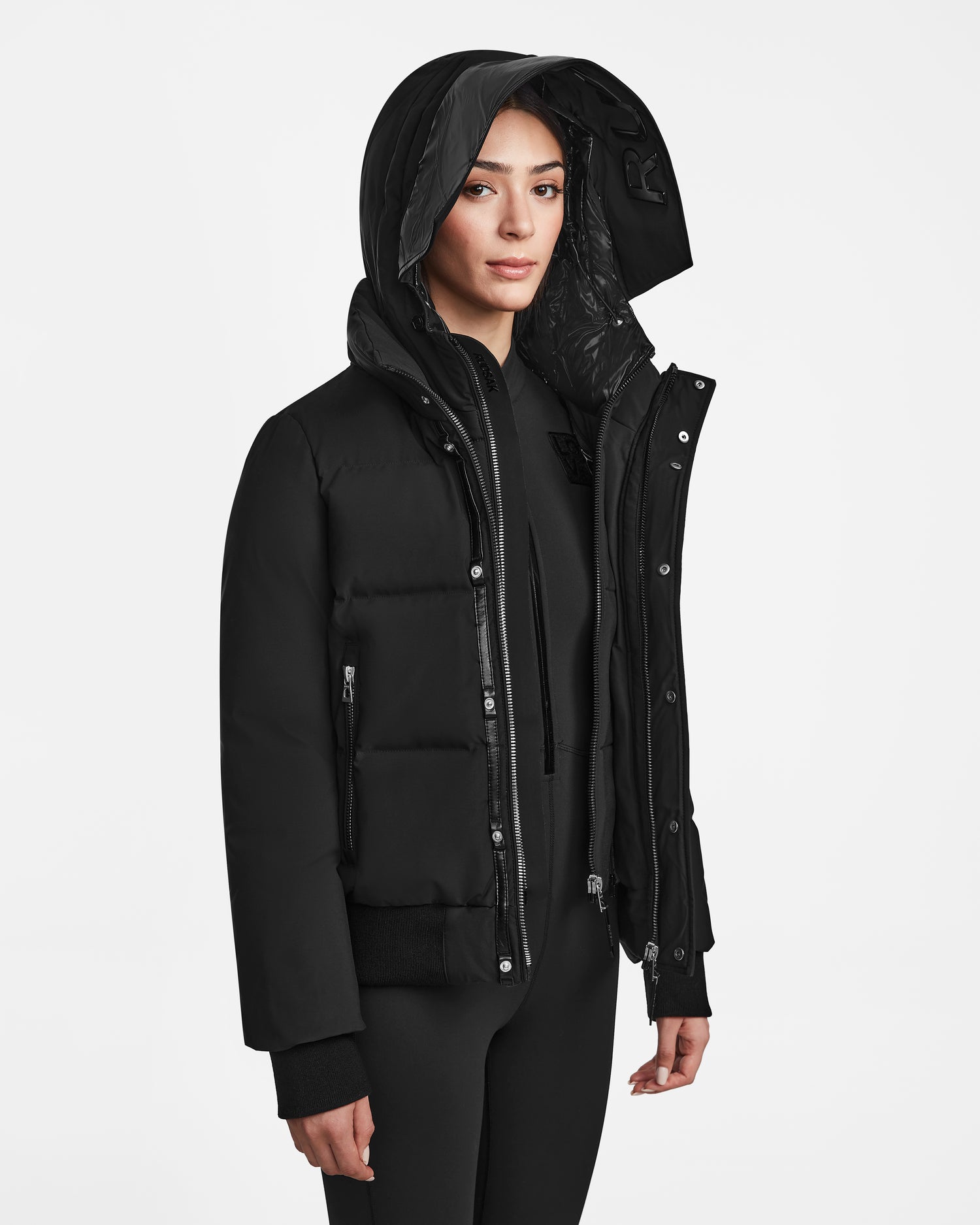 A woman wearing the Rudsak JORDY - 9123513 Black W jacket over a black hoodie stands against a plain white background, looking at the camera with a neutral expression.