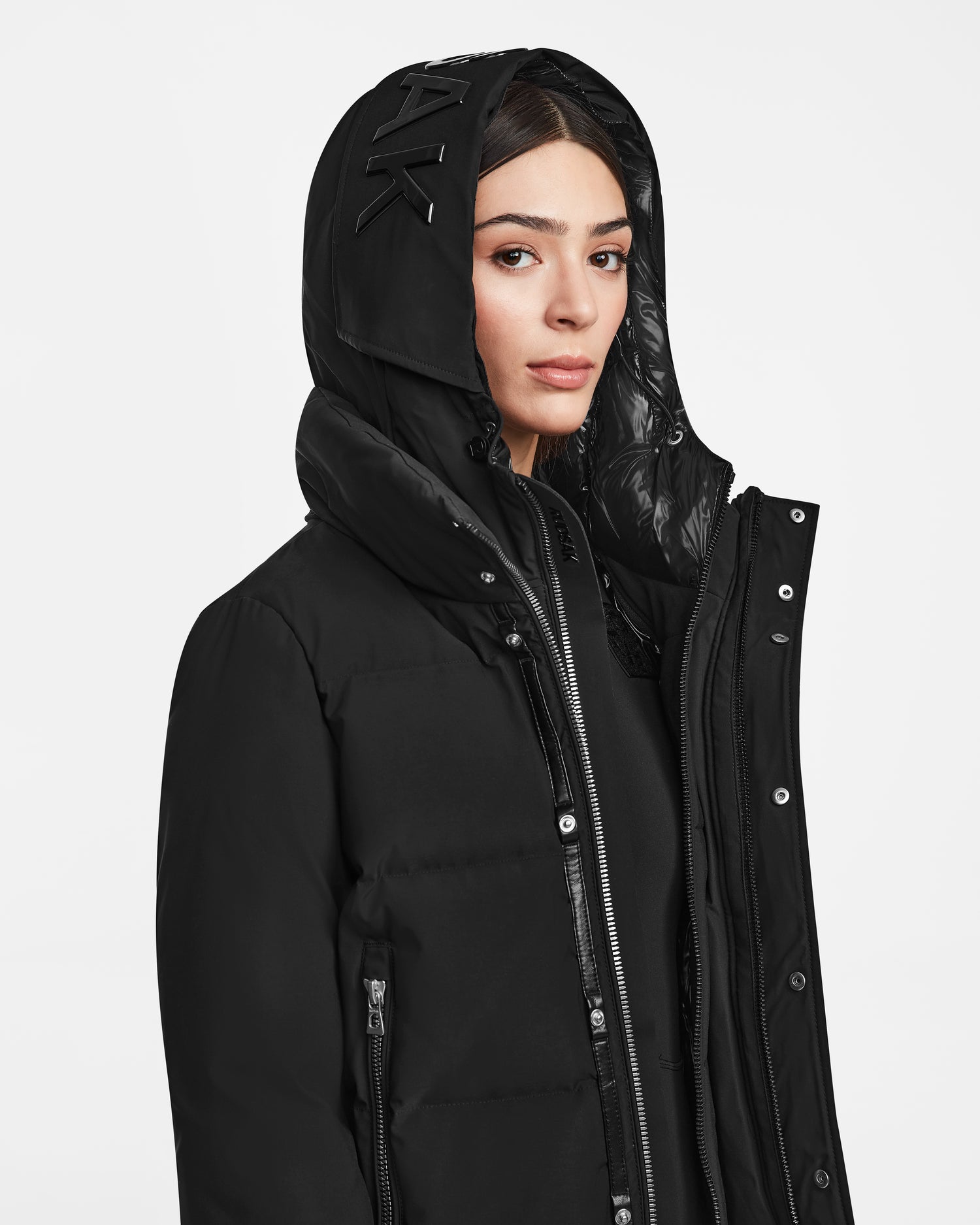 A woman wearing the Rudsak JORDY - 9123513 Black W recycled stormshell jacket with a high collar stands against a plain white background, gazing slightly to the side with a neutral expression.