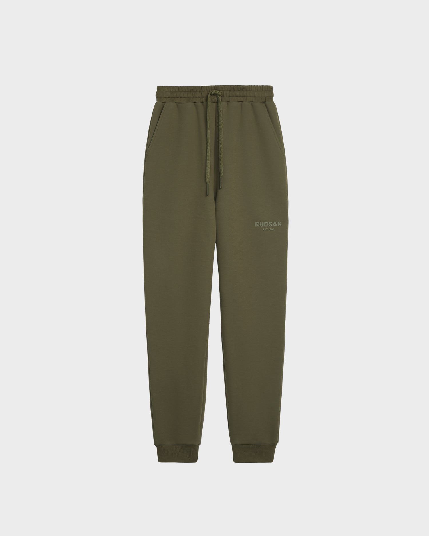 The JOSS - 9524009 Loden Green W unisex jogger sweatpants by Rudsak are crafted from a premium cotton blend with an elastic waistband, drawstring, side pockets, and ribbed cuffs. Rudsak branding is subtly printed on the upper left thigh. Displayed on white background.