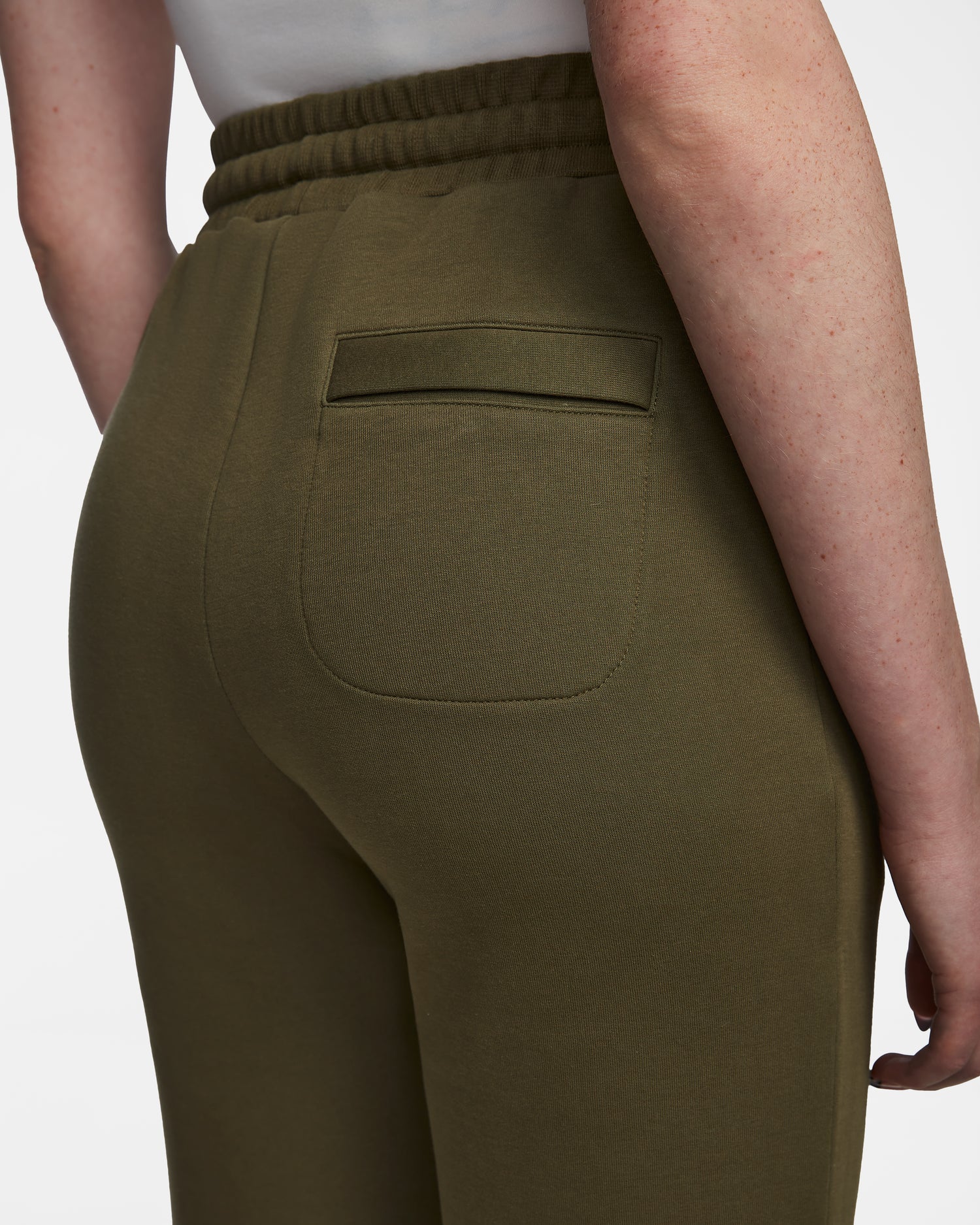 A close-up of a person wearing Rudsak JOSS - 9524009 Loden Green W joggers, featuring an elastic waistband and back pocket, made from a premium cotton blend, with part of their arm and torso visible against a white background.