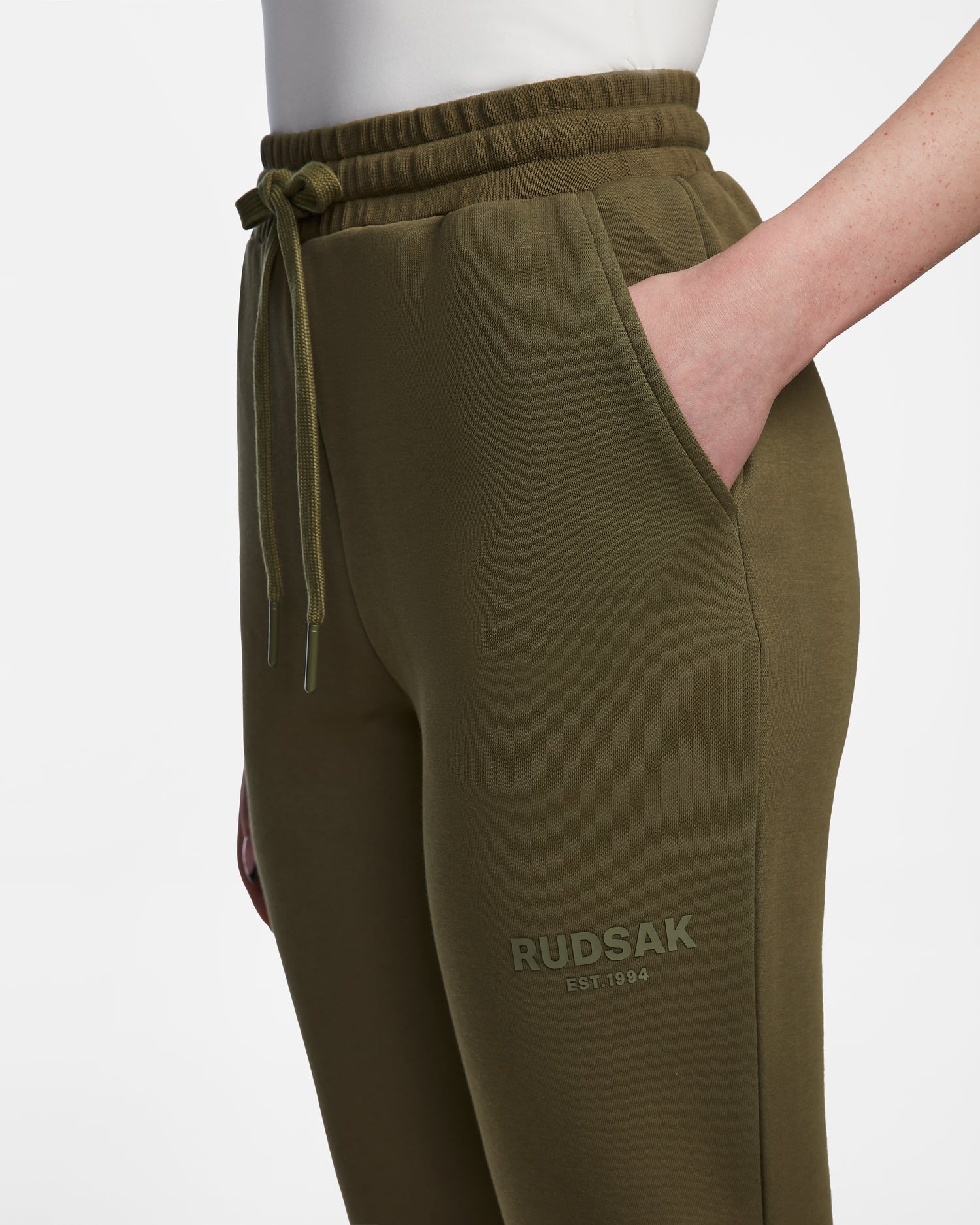 A person wears Rudsak’s JOSS - 9524009 joggers in loden green with an elastic waistband, drawstring, side pockets, and “RUDSAK EST. 1994” printed near the left pocket. Shown on a white background.