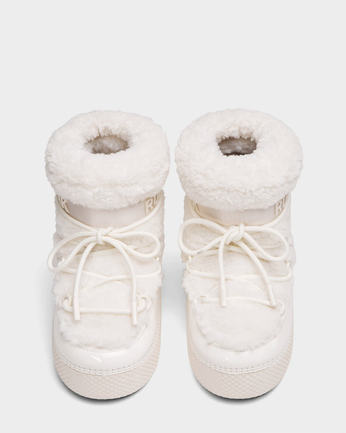 The Rudsak KATHY Y - 1224500 Iceland boots are white, furry winter boots with thick soles, round toes, front laces, and a plush sherpa-like finish. Water-repellent moon boots shown side by side on a white background.
