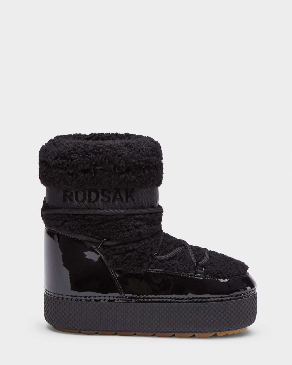 The KATHY - 8223513 Black by Rudsak is a women's winter boot featuring a thick sole, patent leather lower, textured fabric upper, branded ankle strap, cozy insulation, and gum-colored water-repellent outsole—ideal for cold weather.