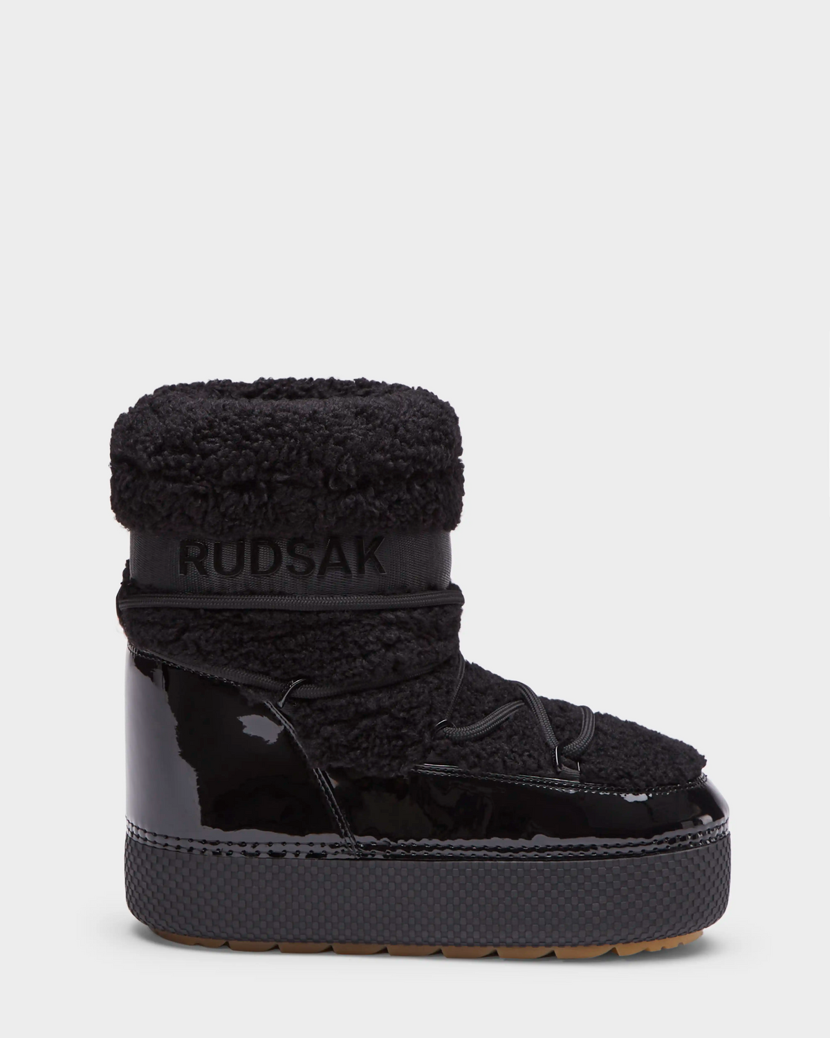 The KATHY - 8223513 Black by Rudsak is a women's winter boot featuring a thick sole, patent leather lower, textured fabric upper, branded ankle strap, cozy insulation, and gum-colored water-repellent outsole—ideal for cold weather.