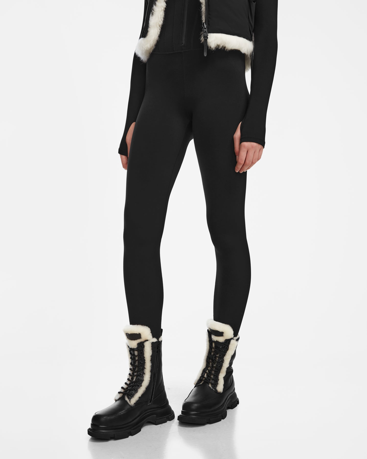 A person stands against a white background wearing black high-waisted leggings, a black long-sleeve top, and Rudsak LANA S - 8224537 Black leather shearling boots with white fur trim. Their face is not visible.