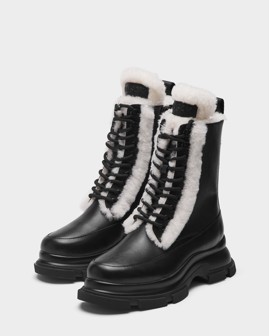 The Rudsak LANA S - 8224537 Black boots feature black leather, thick soles, and white shearling lining along the tongue and edges, shown on a plain white background.