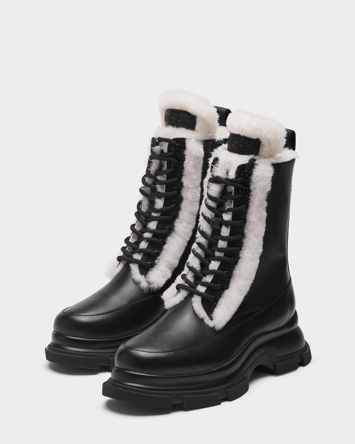 The Rudsak LANA S - 8224537 Black boots feature black leather, thick soles, and white shearling lining along the tongue and edges, shown on a plain white background.