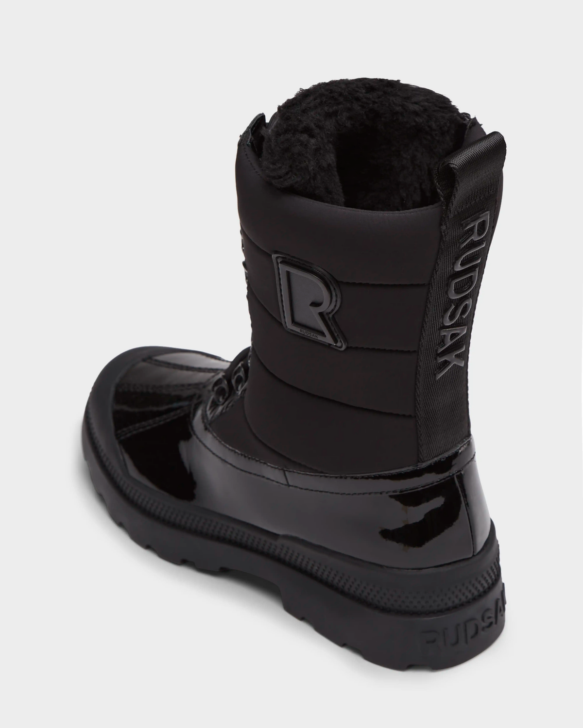 The Rudsak LEX - 8224534 Black is a shiny black women’s winter boot with fur lining, thick sole, water-resistant finish, and RUDSAK branding on the back pull tab, side, plus a visible R logo—combining style and warmth for cold weather.