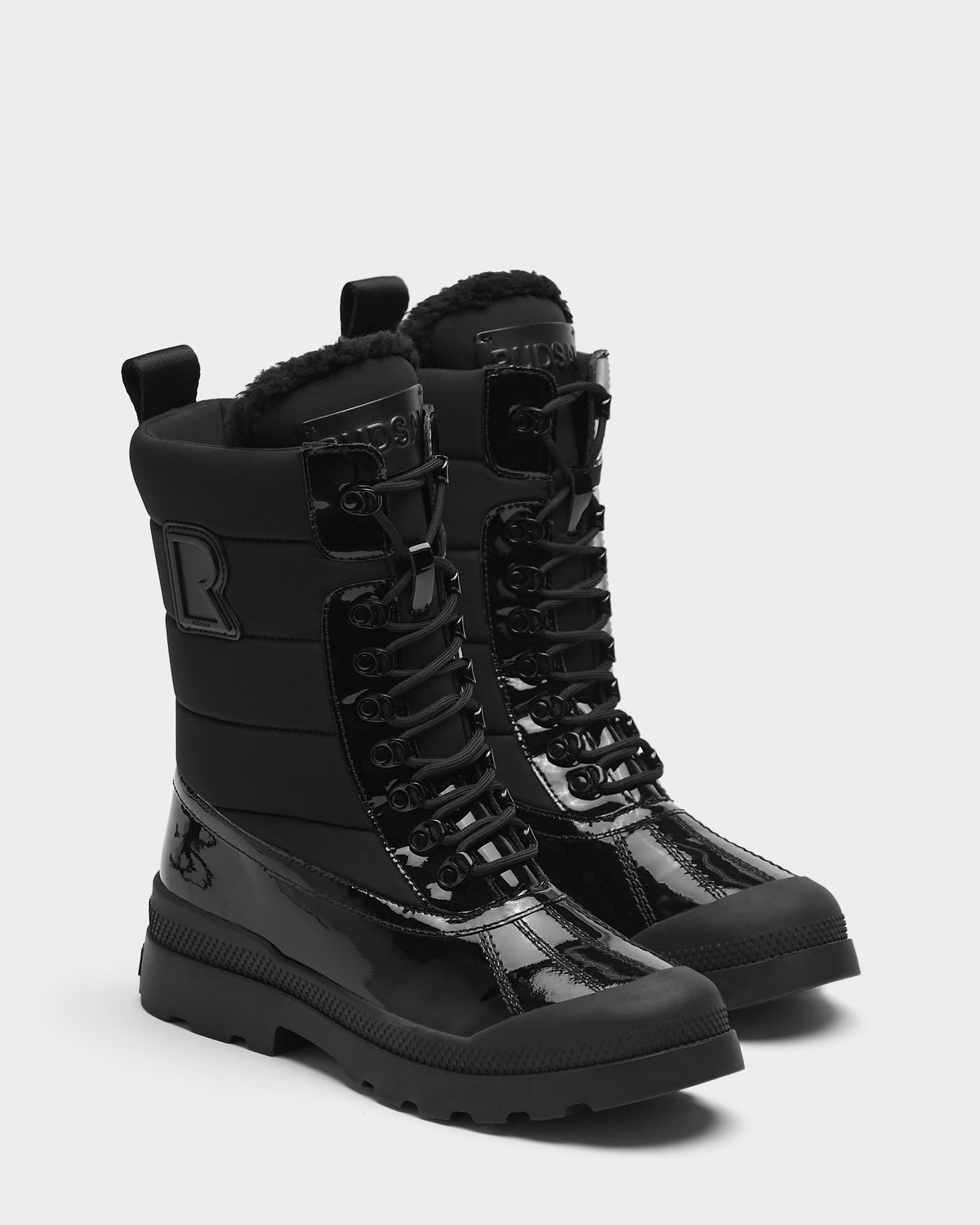 The Rudsak LEX - 8224534 Black women’s winter boots feature shiny patent leather details, lace-up design, thick rubber soles, and warm padded uppers, shown against a plain light background.