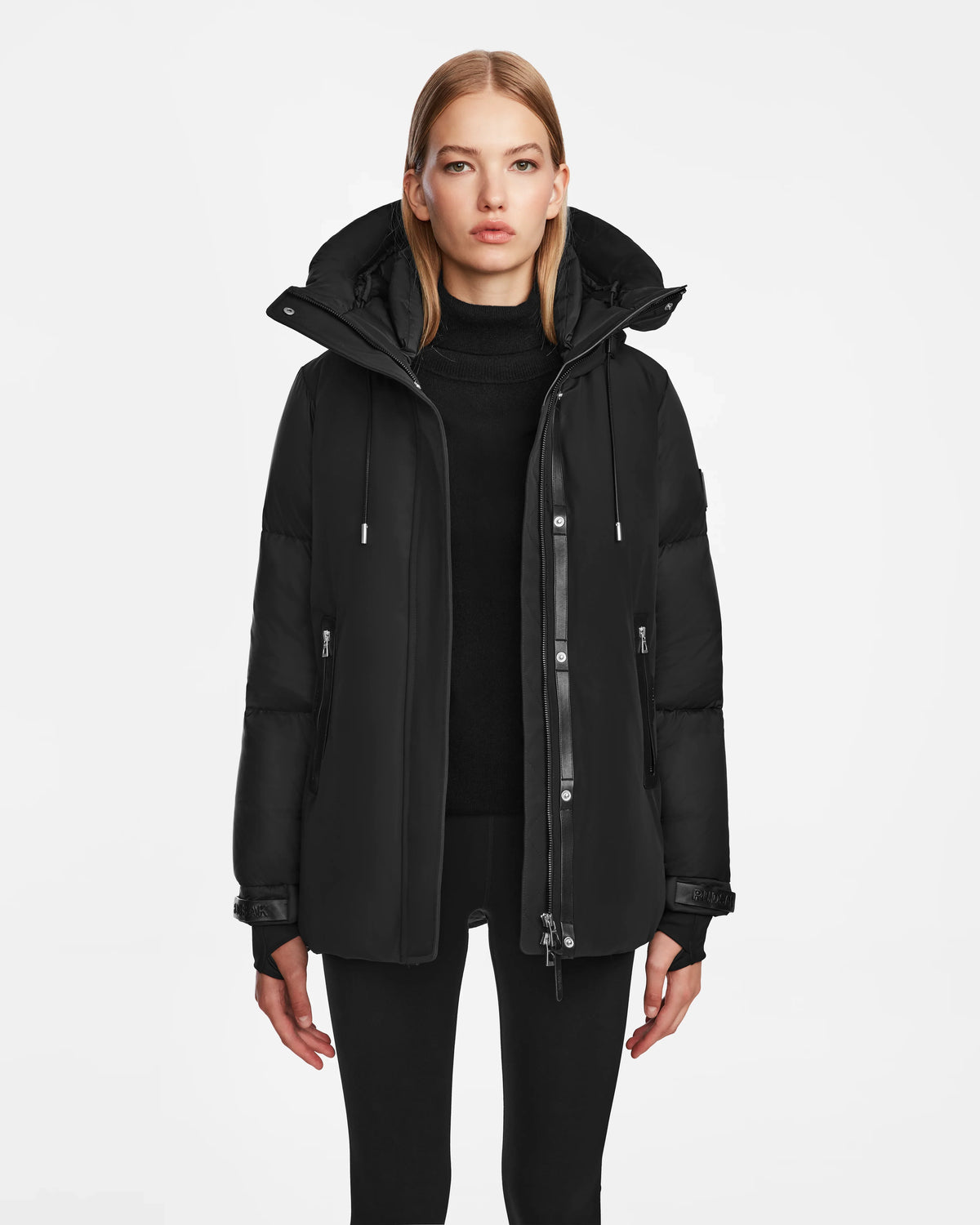 A woman with straight blonde hair wears the Rudsak LOLI - 8124507 Black parka and black pants, standing against a plain white background and looking directly at the camera with a neutral expression.
