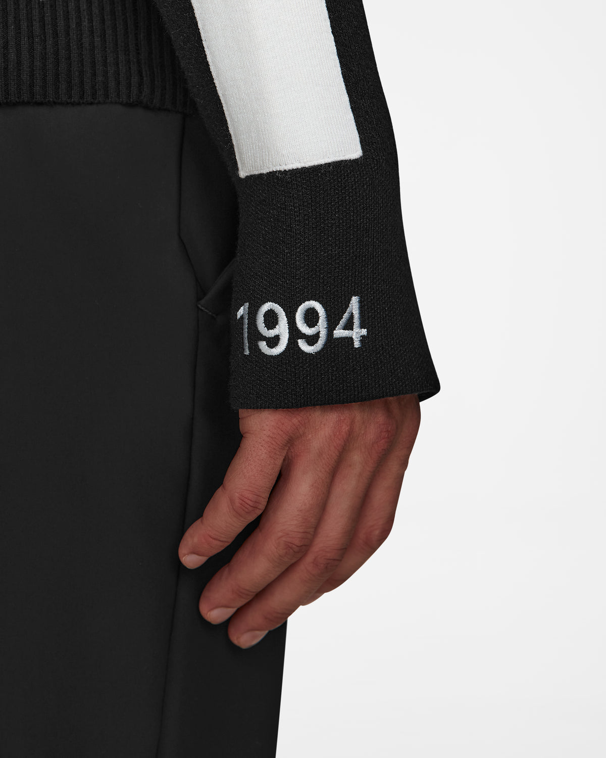 A close-up of a person wearing the Rudsak LUKAS - 6524543 Black mens knit turtleneck sweater with 1994 embroidered on the sleeve, paired with black pants.