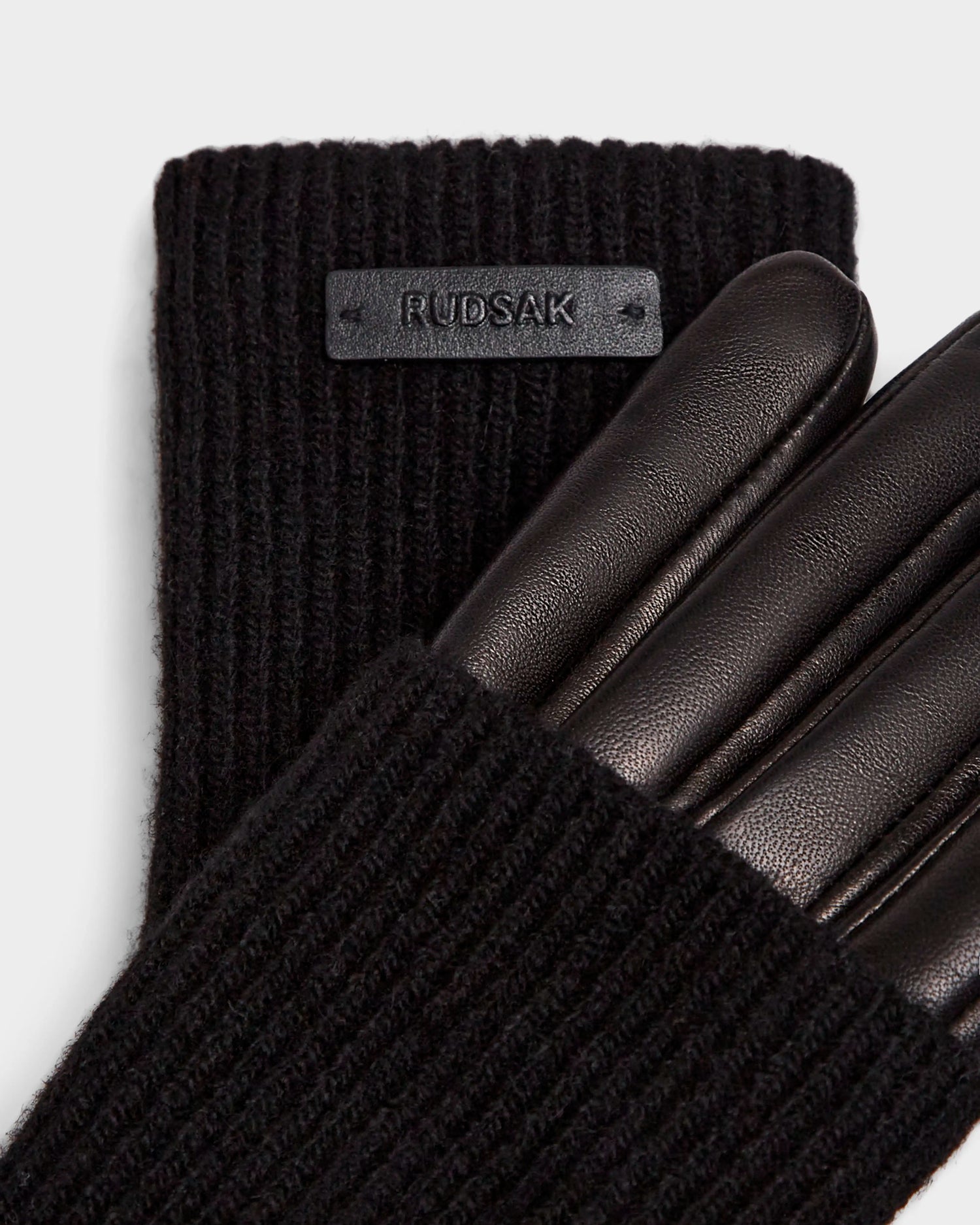 Close-up of MARINE - 8424516 Black womens leather gloves by Rudsak. These chic fall accessories feature ribbed knit cuffs, smooth leather fingers, a black Rudsak tag on the cuff, and a warm wool lining.