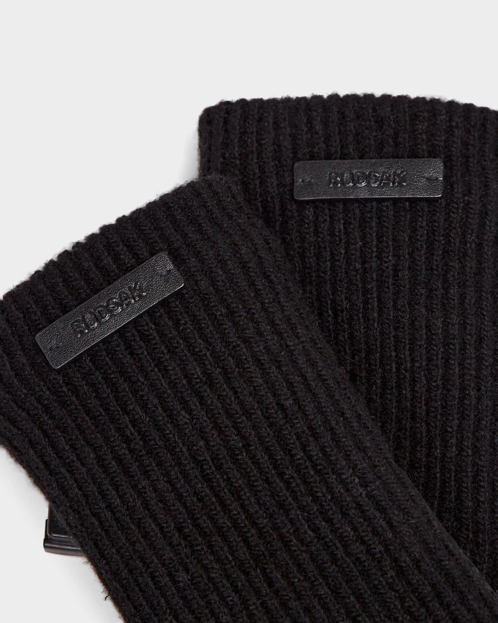 Close-up of two ribbed black knit wool gloves, each with a small rectangular black label stitched on that reads Rudsak—a chic winter accessory: MARINE - 8424516 Black/Black.