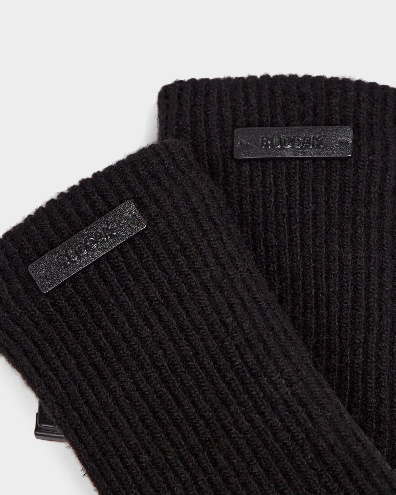 Close-up of two black ribbed knit gloves by Rudsak, the MARINE - 8424516 Black. Each features a small rectangular black label. The chic fall accessories highlight the detailed texture of the knit fabric.