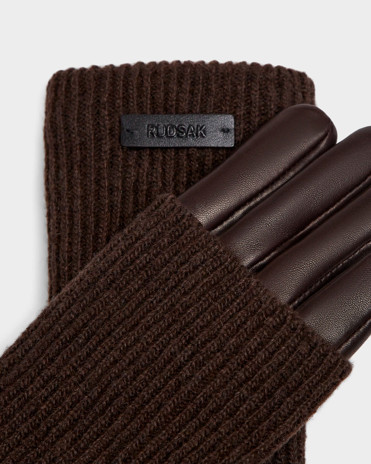 A close-up of an espresso brown MARINE - 8424516 knit glove by Rudsak shows a leather palm and fingers, ribbed pattern, wool lining for warmth, and the black Rudsak label on the wrist.