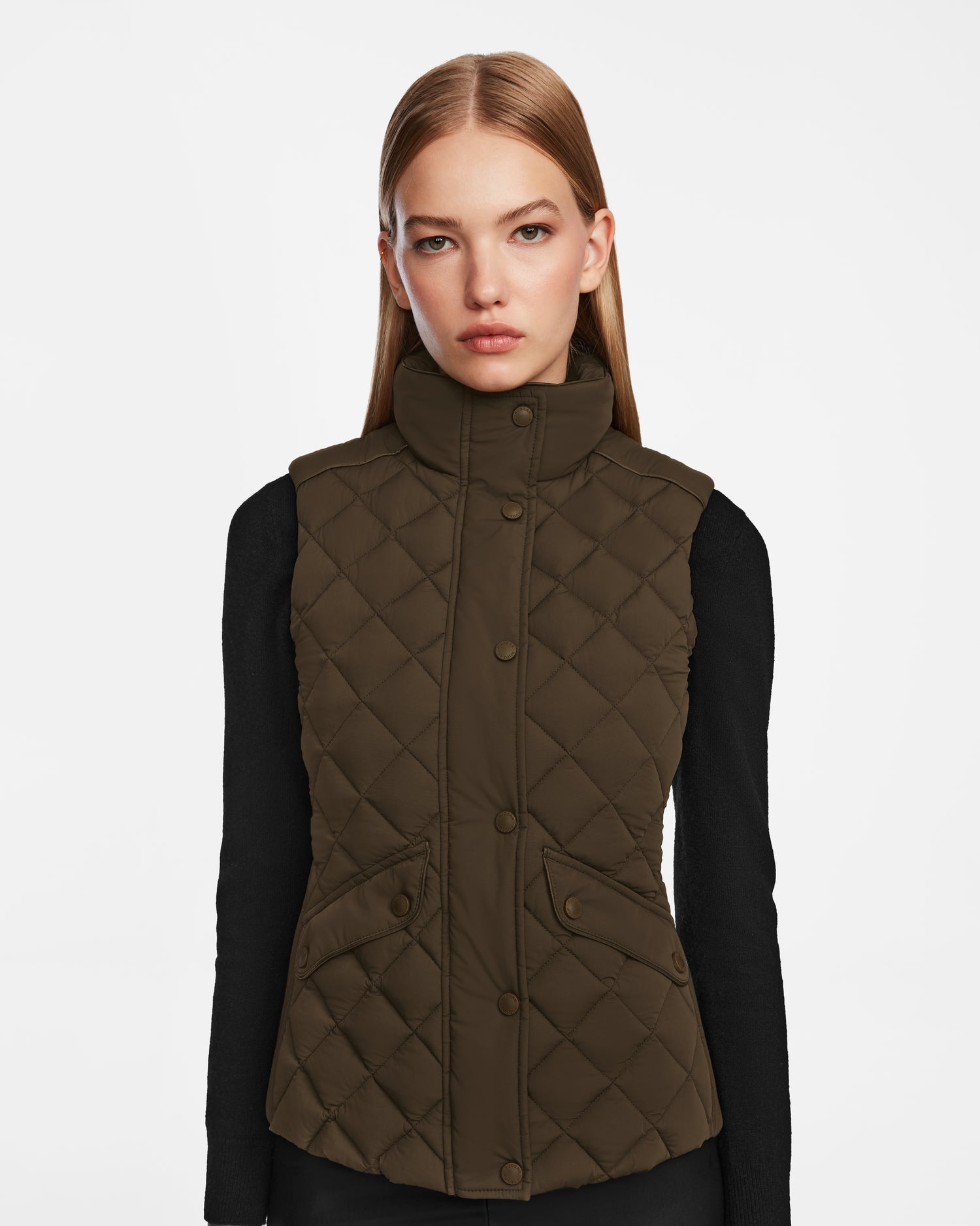 A woman with straight, light brown hair models the Rudsak MATILDA - L124504 Army dark olive womens vest over a black long-sleeve top against a plain white background.