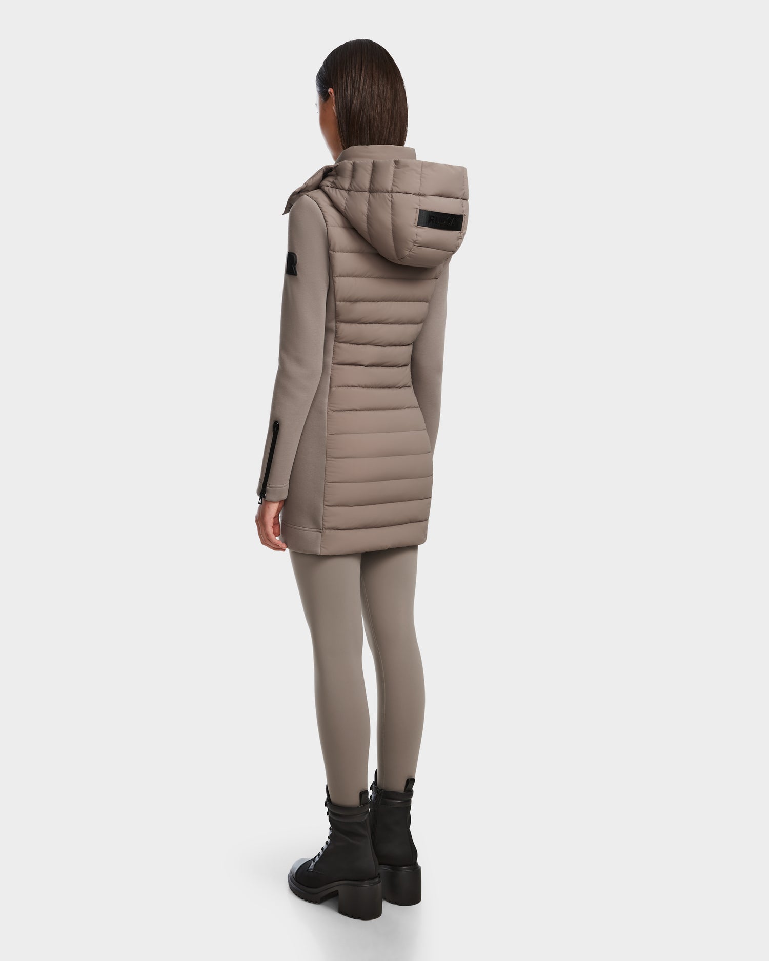 A person wearing the Rudsak MERINA M - 8124030 Cement women’s light hooded jacket, matching leggings, and black chunky boots stands facing away against a white background.