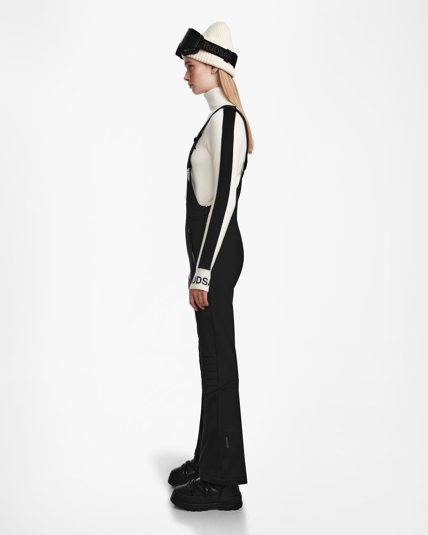 A woman in a black and white outfit showcases the NANOR - 8124819 Black fitted flared ski pants by Rudsak, blending fashion and function for the slopes.