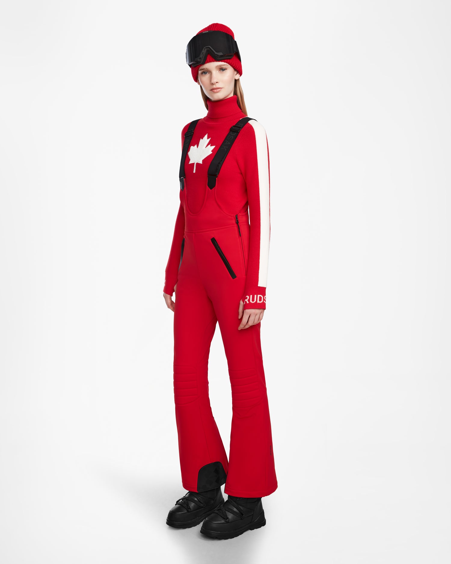 A woman in a red outfit showcases the Rudsak NANOR - 8124819 Flame Red fitted flared ski pant, blending style and function with women’s ski pants enhanced by RECCO rescue technology.