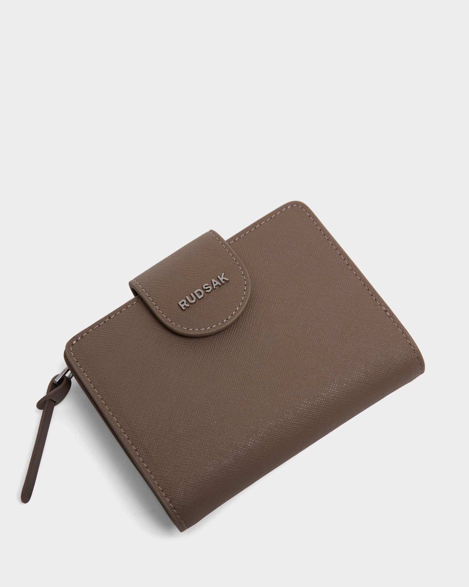 The NOVALIE - L424500 Sand is a brown textured womens leather cardholder by Rudsak, featuring a snap closure, zipper compartment, and embossed branding on the front—all shown against a plain white background.
