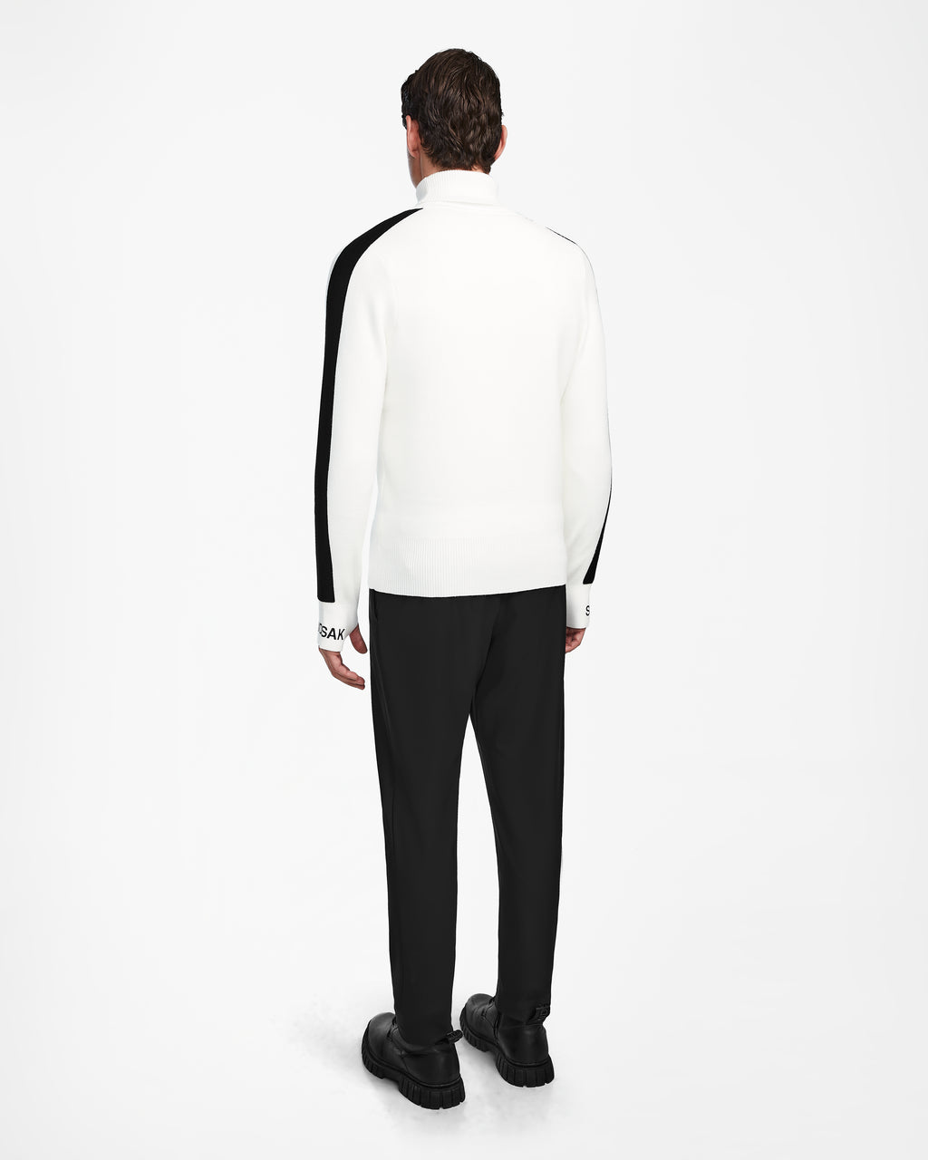 A person stands facing away, wearing Rudsaks OLIVIER - 6524545 Optic White mens ski turtleneck—white with black sleeve stripes—paired with black pants and shoes, against a plain white background; ideal for any winter wardrobe.