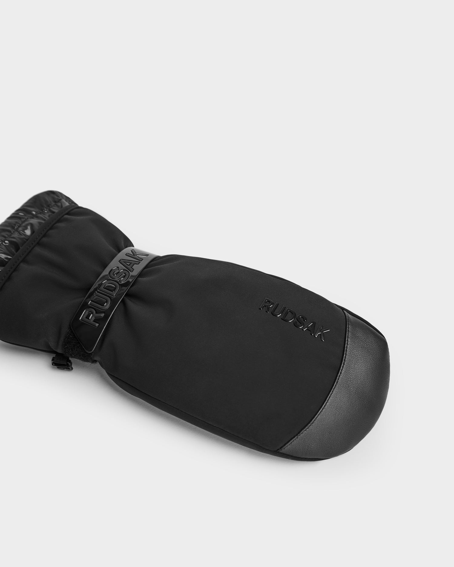 A single OLTEN - 9425565 Black ski mitten by Rudsak, with branding on top, a smooth exterior, and leather accents at the thumb and cuff, shown on a plain light gray background.