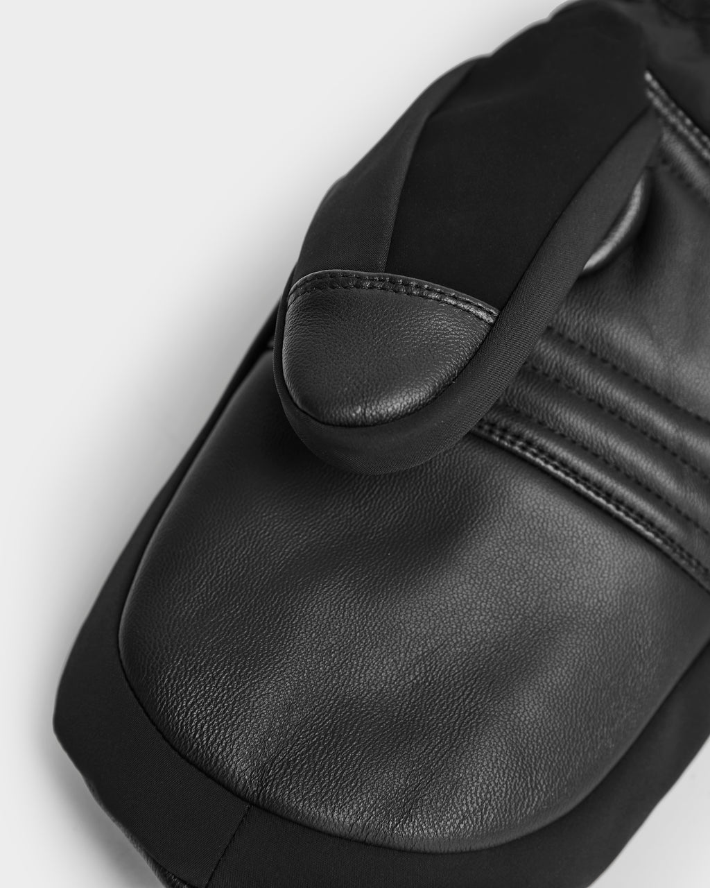 A close-up of Rudsak's OLTEN - 9425565 Black mitten shows textured leather palms, visible stitching, and fabric accents, emphasizing the quality craftsmanship of these insulated winter gloves against a light background.