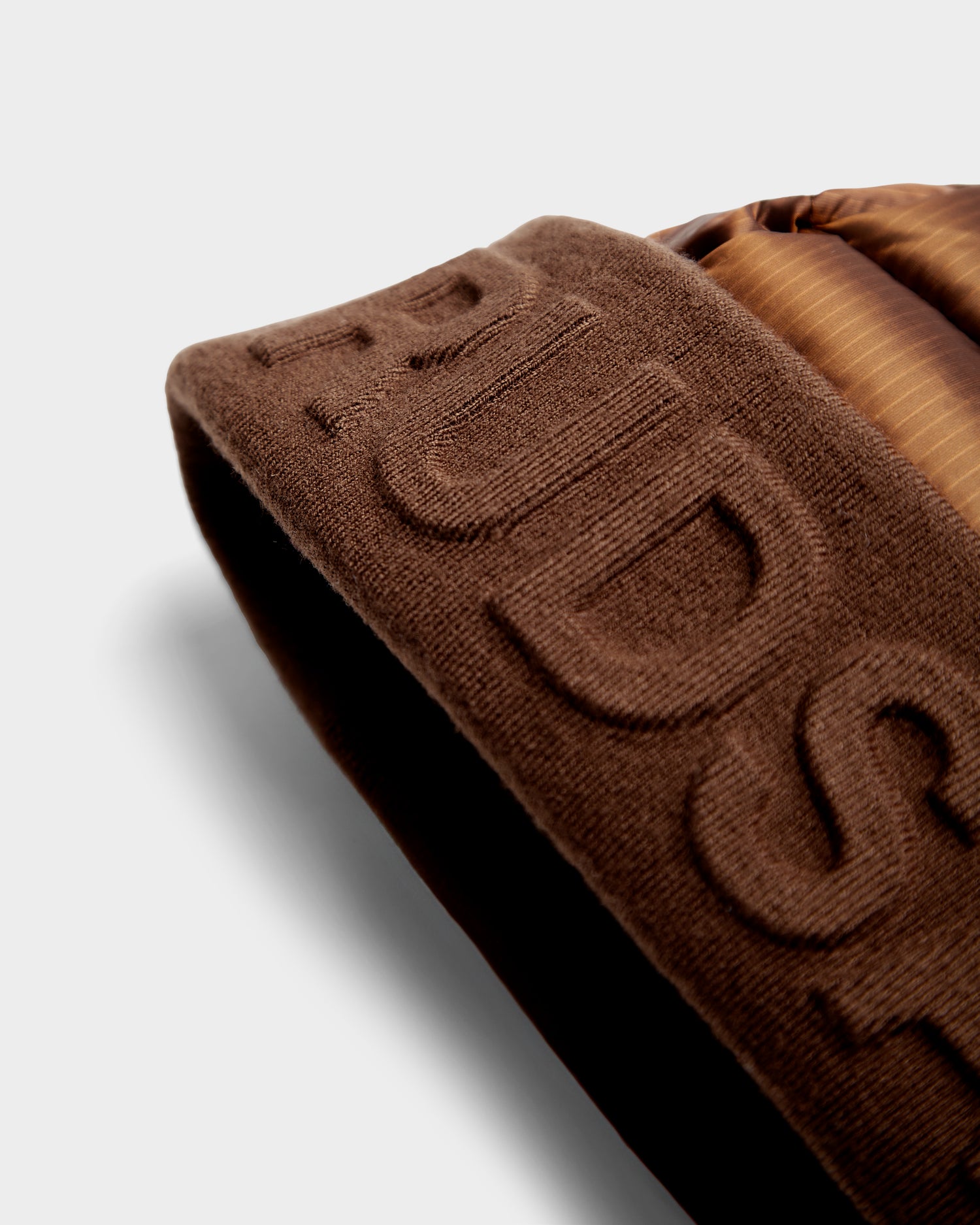 Close-up of the Rudsak OLYA - 8422504 Antique Bronze, showing brown knit fabric with raised embroidery and a section of shiny, quilted RDS-certified down, set against a light background.