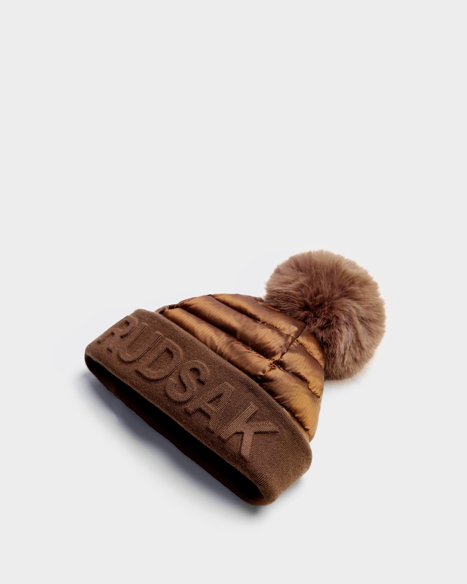 The Rudsak OLYA - 8422504 Antique Bronze women’s winter hat features a large fluffy pom-pom and an embroidered logo on the folded brim, shown against a plain white background.