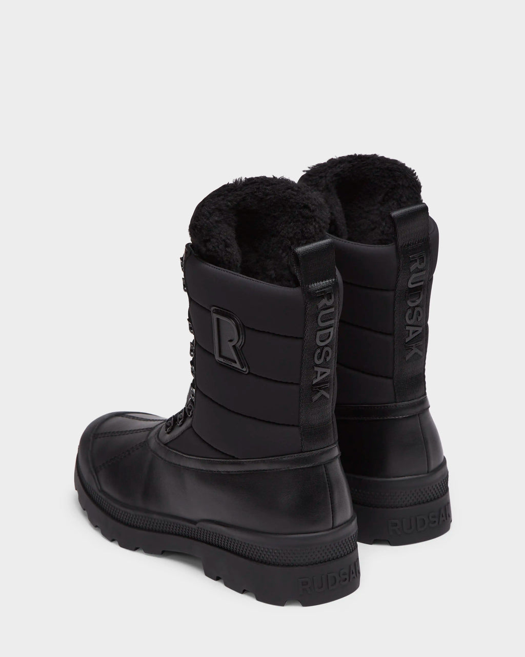 The Rudsak REAGAN - 6224501 Black men’s winter boots feature thick soles, lace-up fronts, soft furry linings, a back pull tab, and the Rudsak name embossed vertically for a stylish finish.