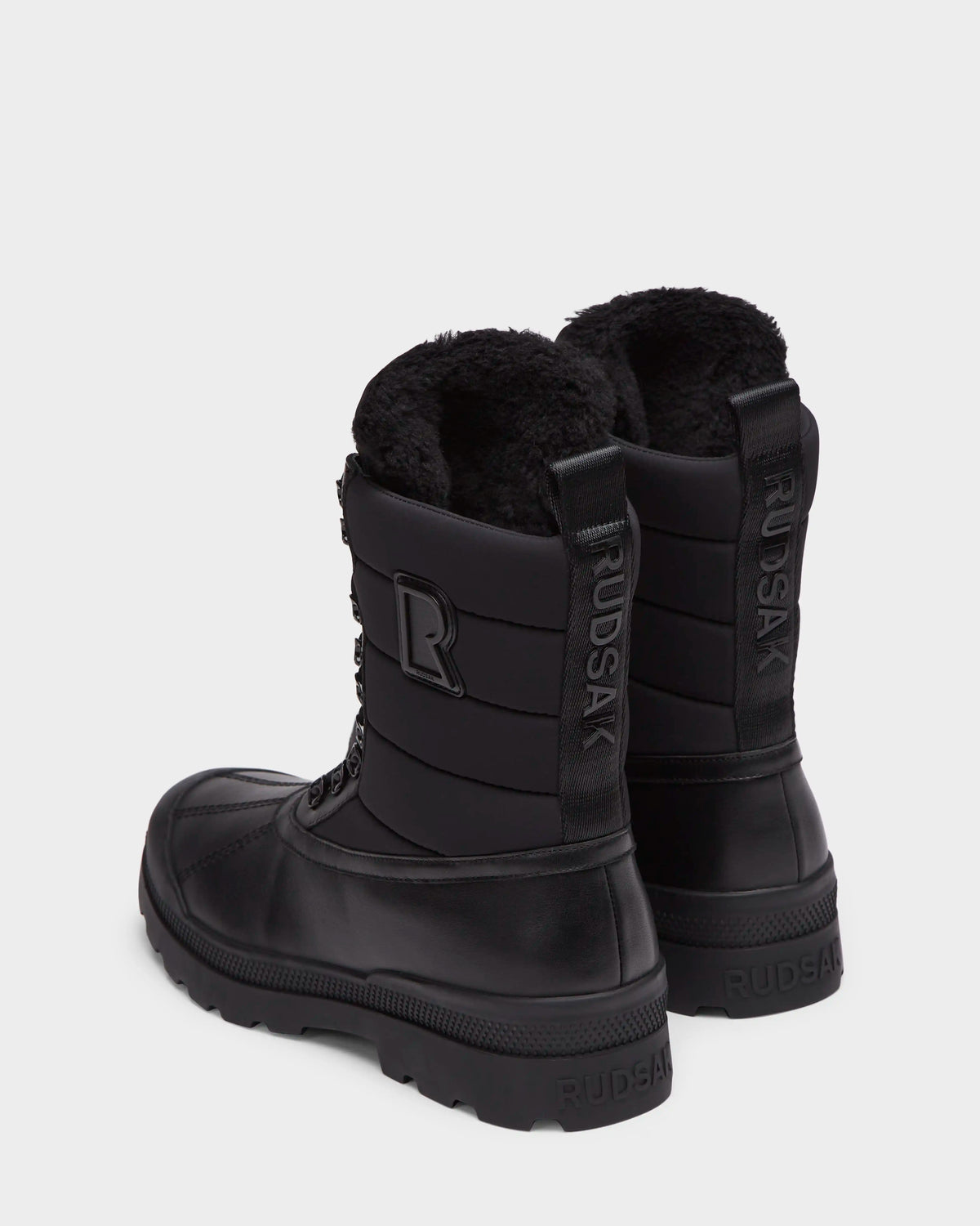 Two black Rudsak REAGAN - 6225046 Black mid-calf men’s winter boots with lug soles, quilted shafts, and black fur lining.