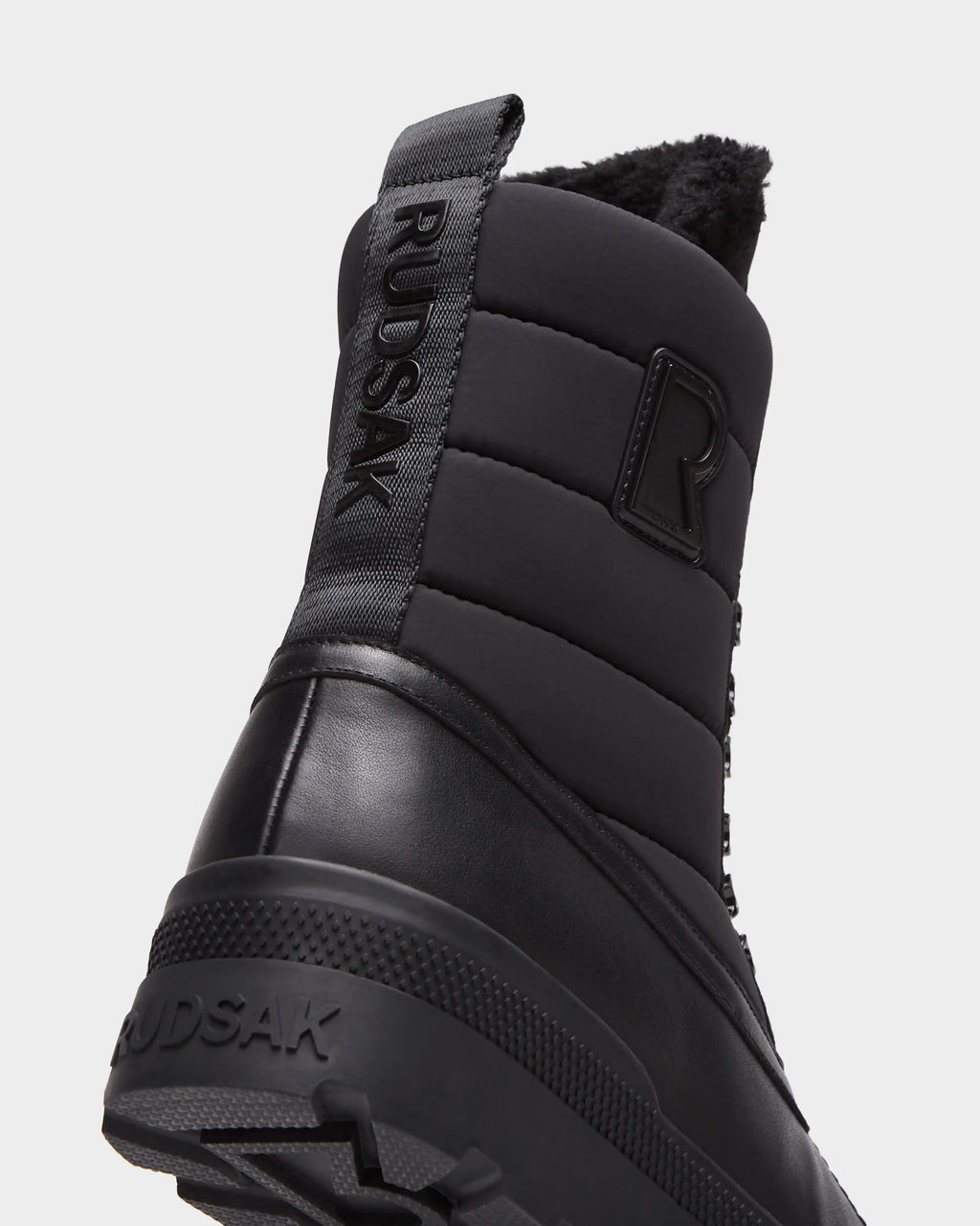 Close-up, rear view of black Rudsak REAGAN - 6225046 Black winter boots featuring a quilted upper, a branded pull tab on the heel, and a textured rubber sole.
