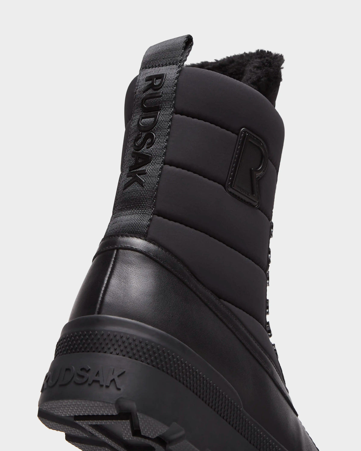 Close-up, rear view of black Rudsak REAGAN - 6225046 Black winter boots featuring a quilted upper, a branded pull tab on the heel, and a textured rubber sole.