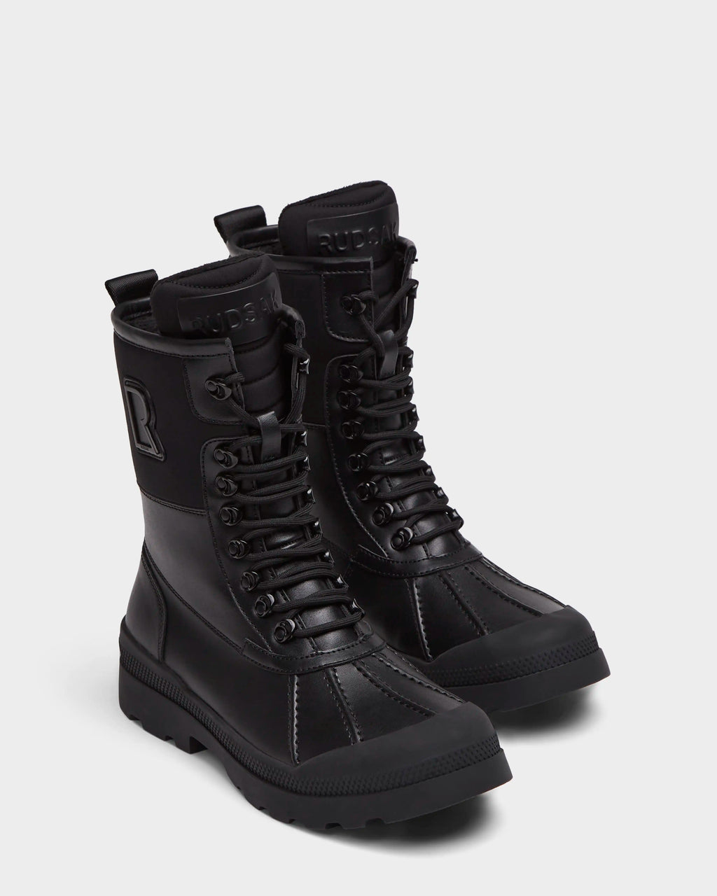 The Rudsak RITA - L222502 Black women's winter boots feature mid-calf lace-up design, weather-treated leather, rugged soles, and embossed branding on the tongue and side, shown on a plain light background.