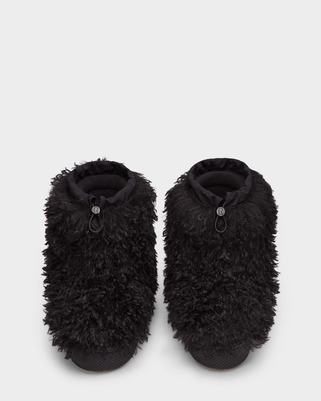 The Rudsak ROSSY - 8224518 Black slippers, inspired by Mongolian fur boots, feature thick, shaggy black faux fur and adjustable drawstring ankle closures, shown against a plain white background.
