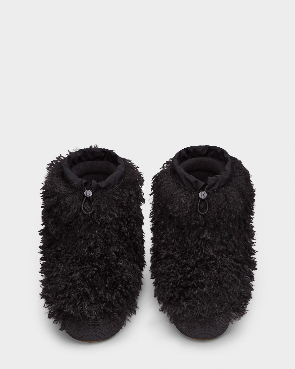 The Rudsak ROSSY - 8224518 Black slippers, inspired by Mongolian fur boots, feature thick, shaggy black faux fur and adjustable drawstring ankle closures, shown against a plain white background.