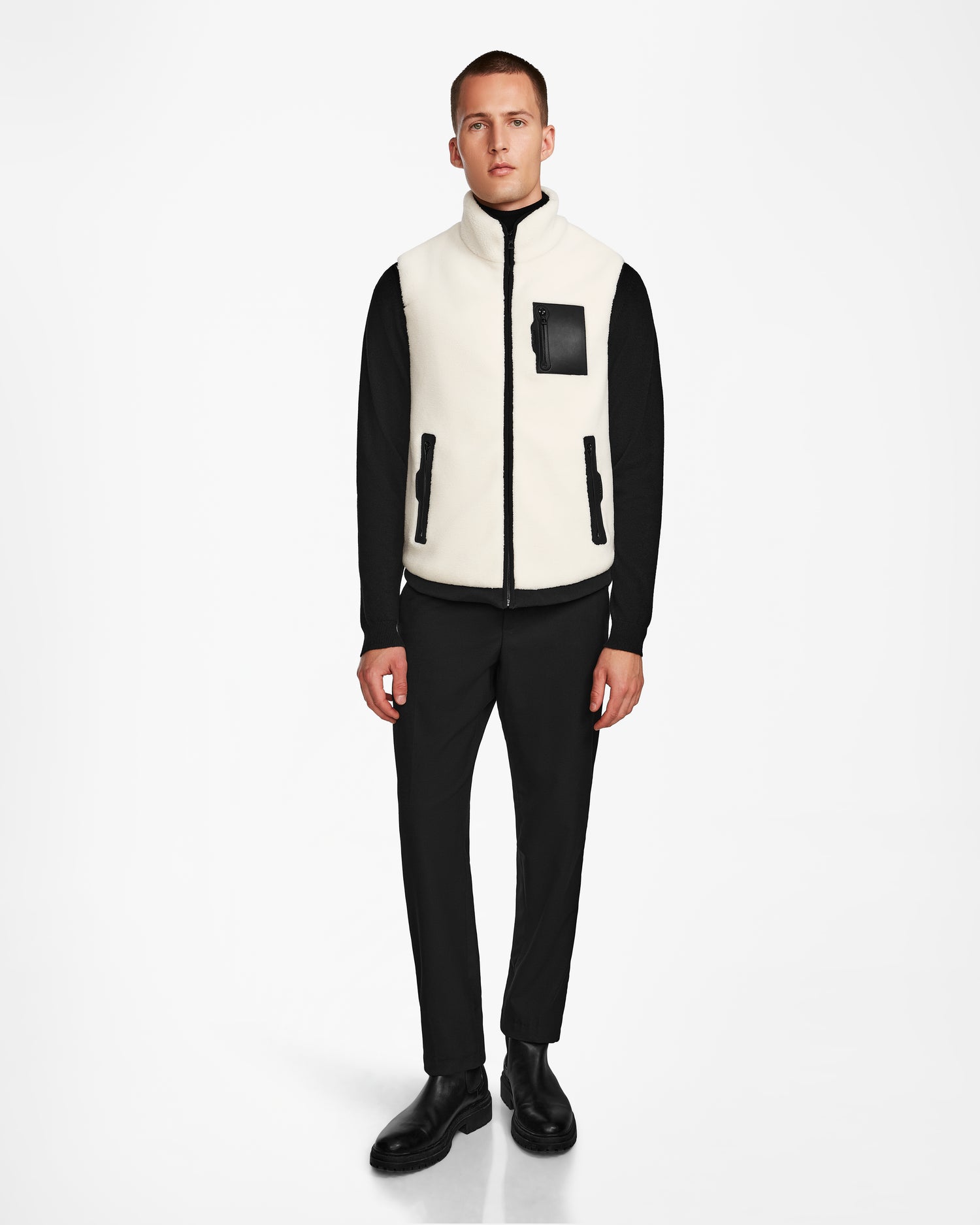 A man faces forward wearing the Rudsak RUMMY - U524502 Iceland M unisex polar fleece vest with black zipper details over a black long-sleeve shirt and pants, set against a plain white background—a true layering essential.