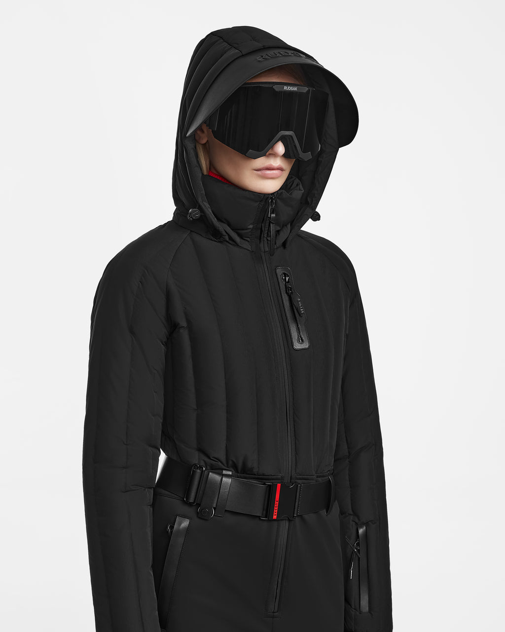 A person wearing the Rudsak SAGE - 8124782 Black hooded jacket with RECCO rescue technology, large black visor sunglasses, and a black belt with a red accent, facing slightly to the side against a plain white background.
