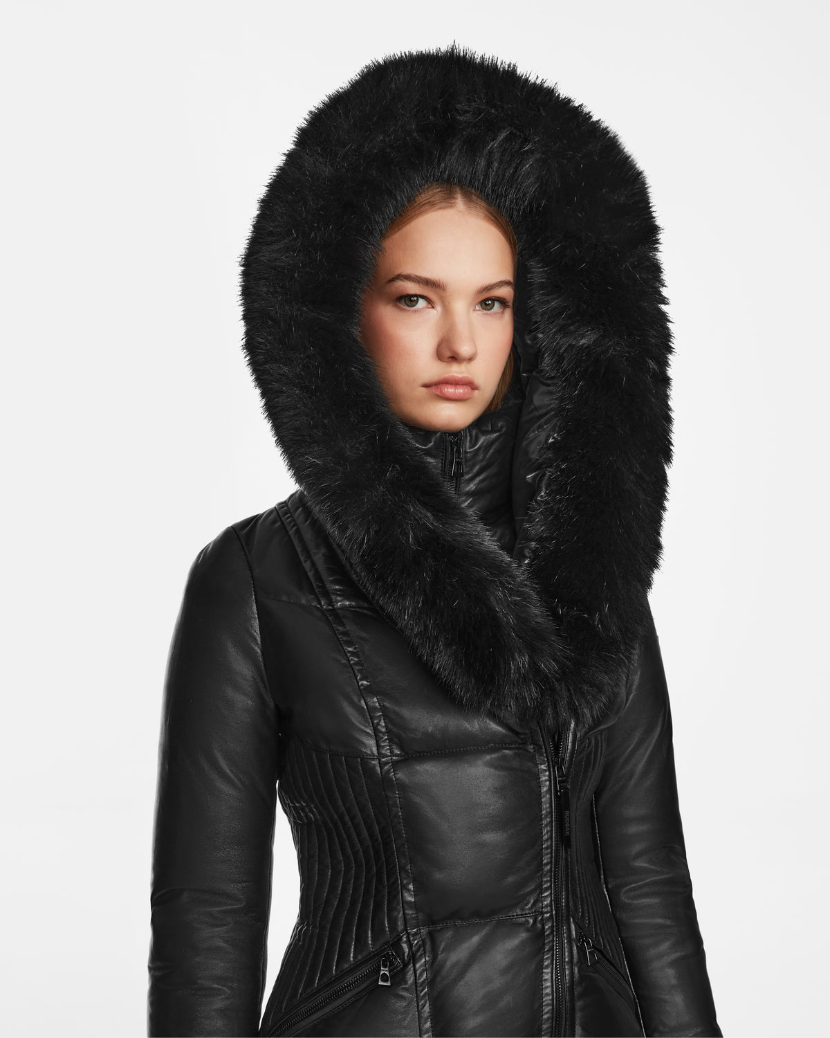 A woman wears the Rudsak SHAUNA X - 8122535 BLACK leather jacket with a large, fluffy fur-trimmed hood, standing against a plain white background.