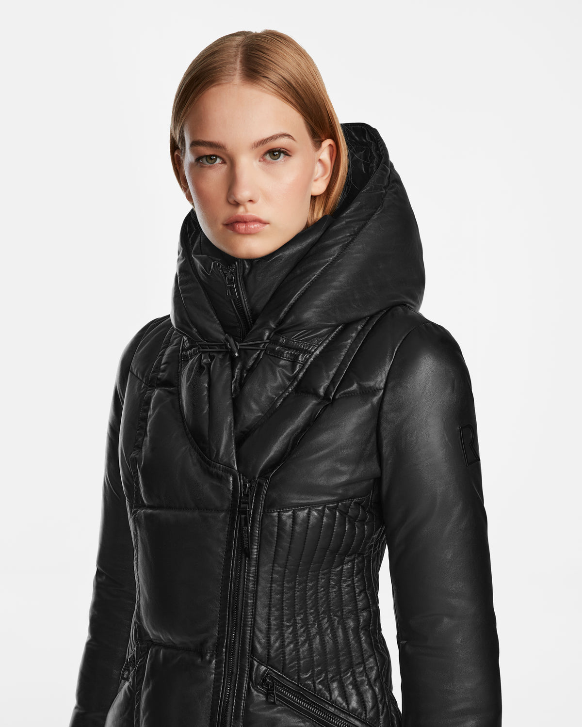 A woman with straight, light brown hair models the Rudsak SHAUNA X - 8122535 BLACK quilted leather jacket with a large, padded collar against a plain white background.
