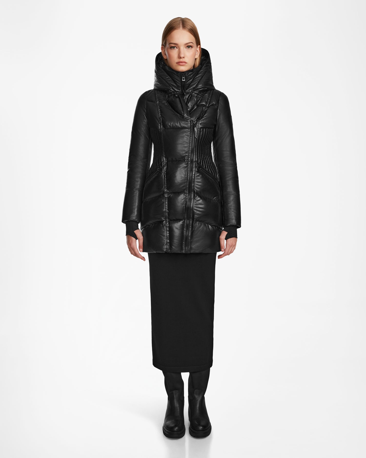A woman faces forward in a shiny black Rudsak SHAUNA X - 8122535 puffer jacket with RDS certified down, high collar and hood, paired with a long black skirt and boots, against a plain white background.