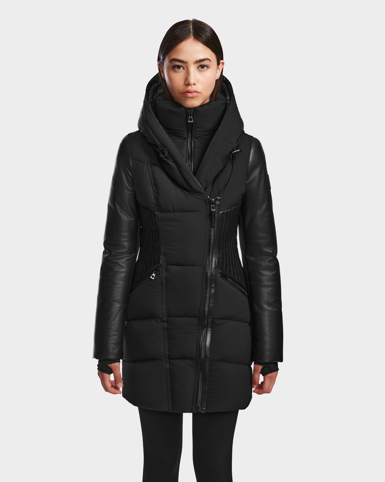 A woman faces forward wearing RUDSAK's SHAUNA - 8122586 BLACK quilted down puffer coat with leather sleeves, zippered pockets, a wide high collar, and fitted silhouette, shown against a plain white background.