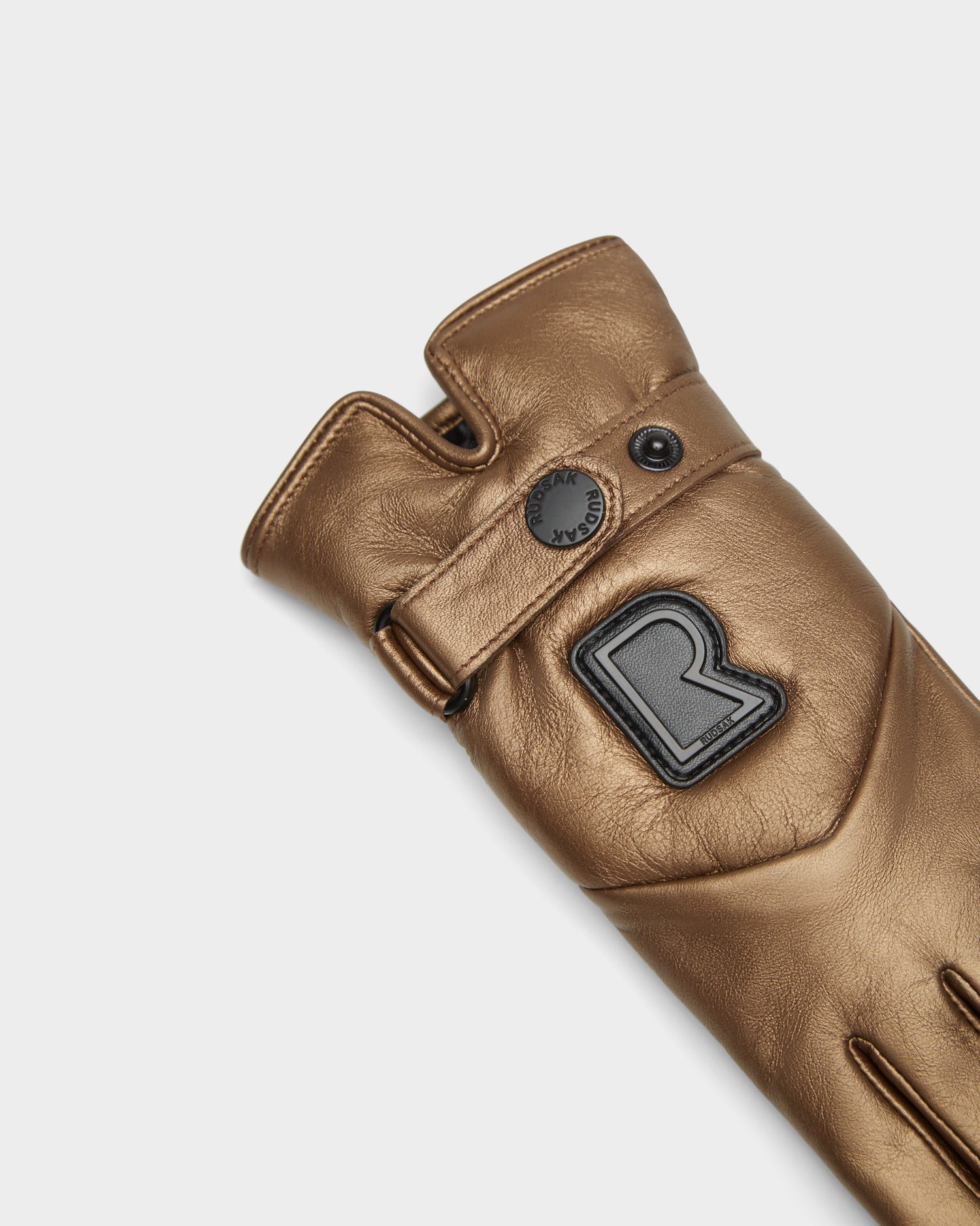 The Rudsak STROMBOLI - 8424510 Antique Bronze women's leather glove features a black R patch, snap button, and knuckle cutout, shown on a plain white background.