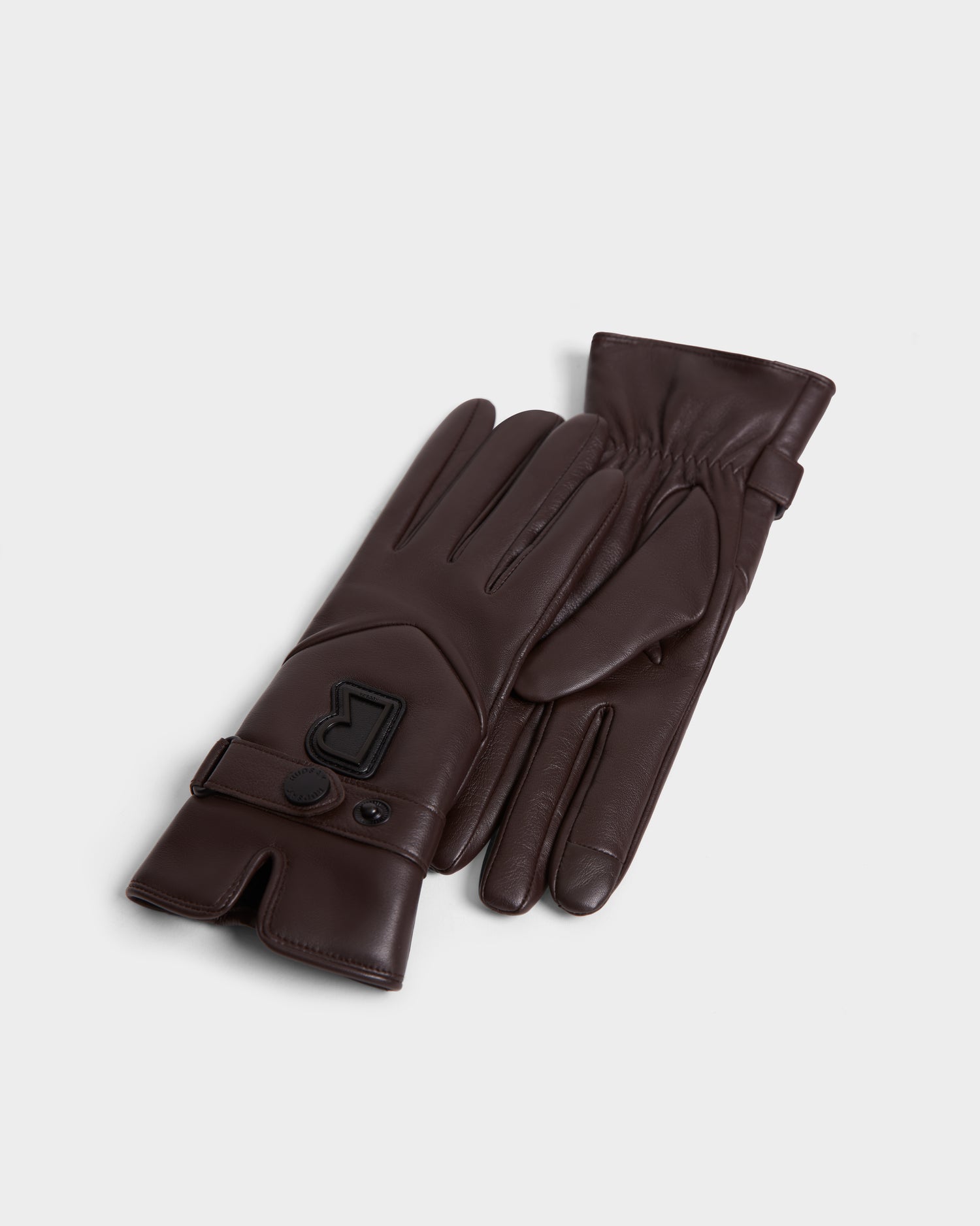The Rudsak STROMBOLI - 8424510 Espresso are dark brown leather cashmere gloves for women, featuring a buttoned strap and raised “R” logo on the wrist, shown on a plain white background.
