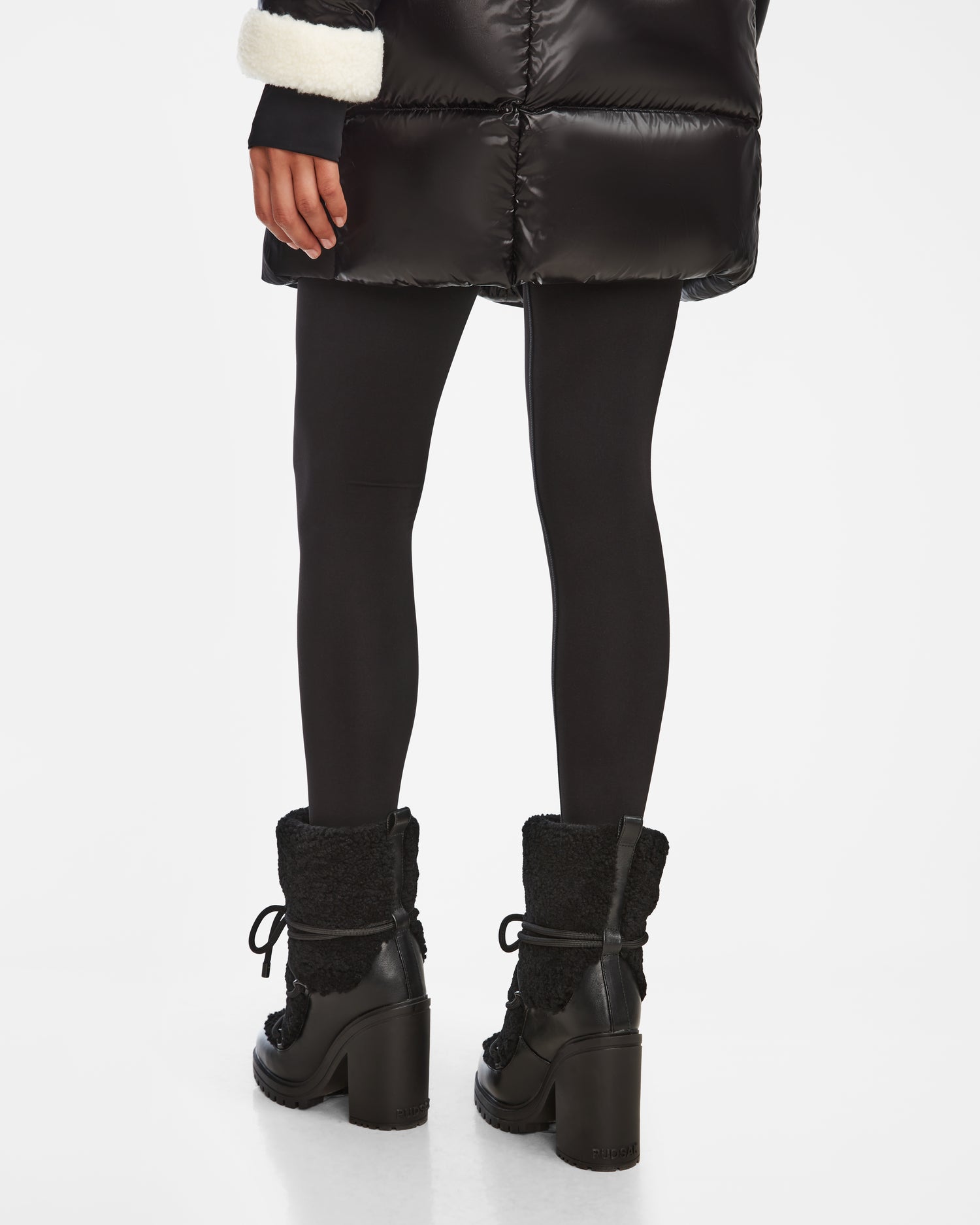A person shown from the back against a white background wears a Rudsak TALYNA - 8224504 Black puffer coat, black leggings, and high-heel lace-up womens ankle boots.