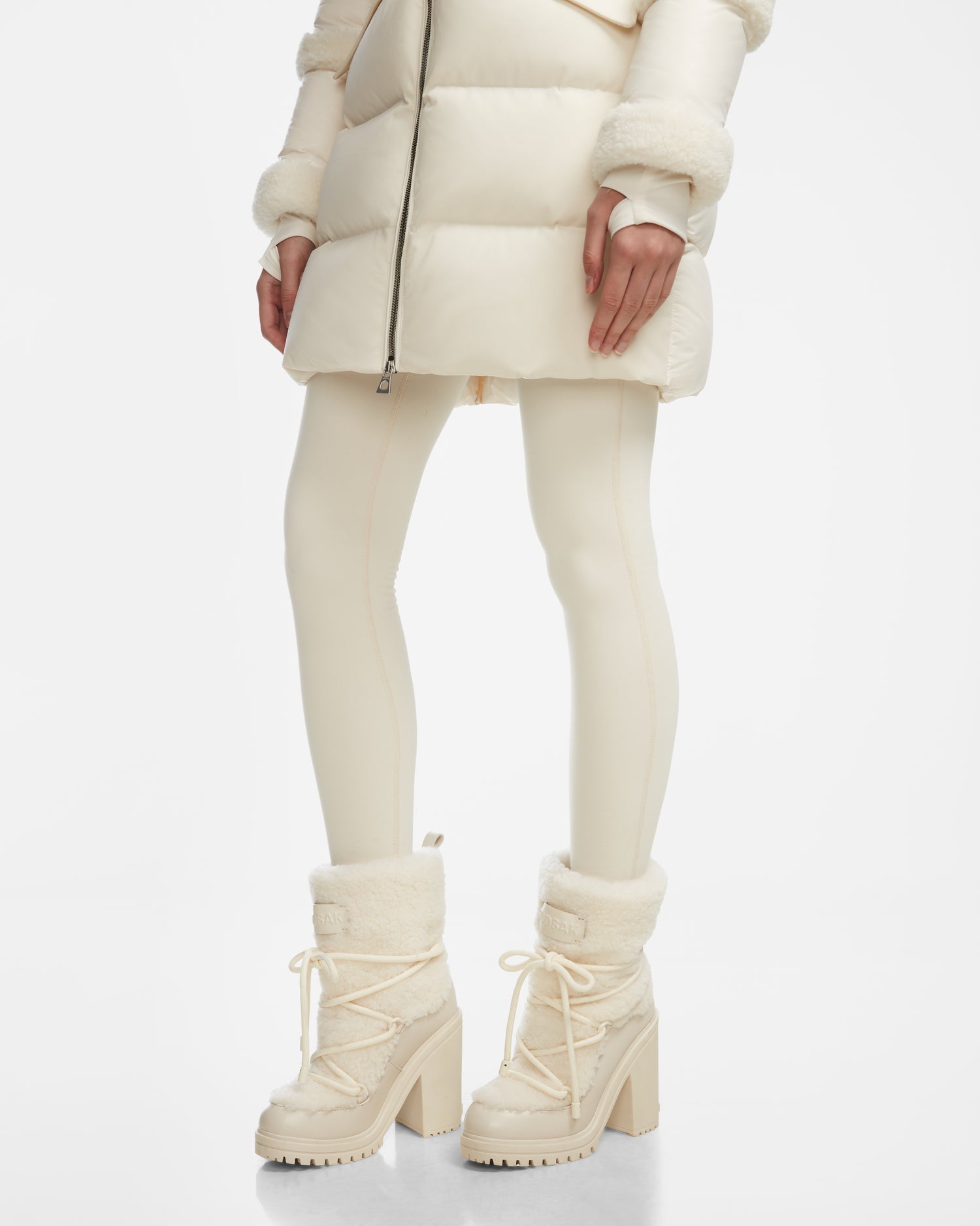 A person models the Rudsak TALYNA - 8224504 Iceland cream puffer coat, matching leggings, and chic fur-trimmed heeled boots against a white background.