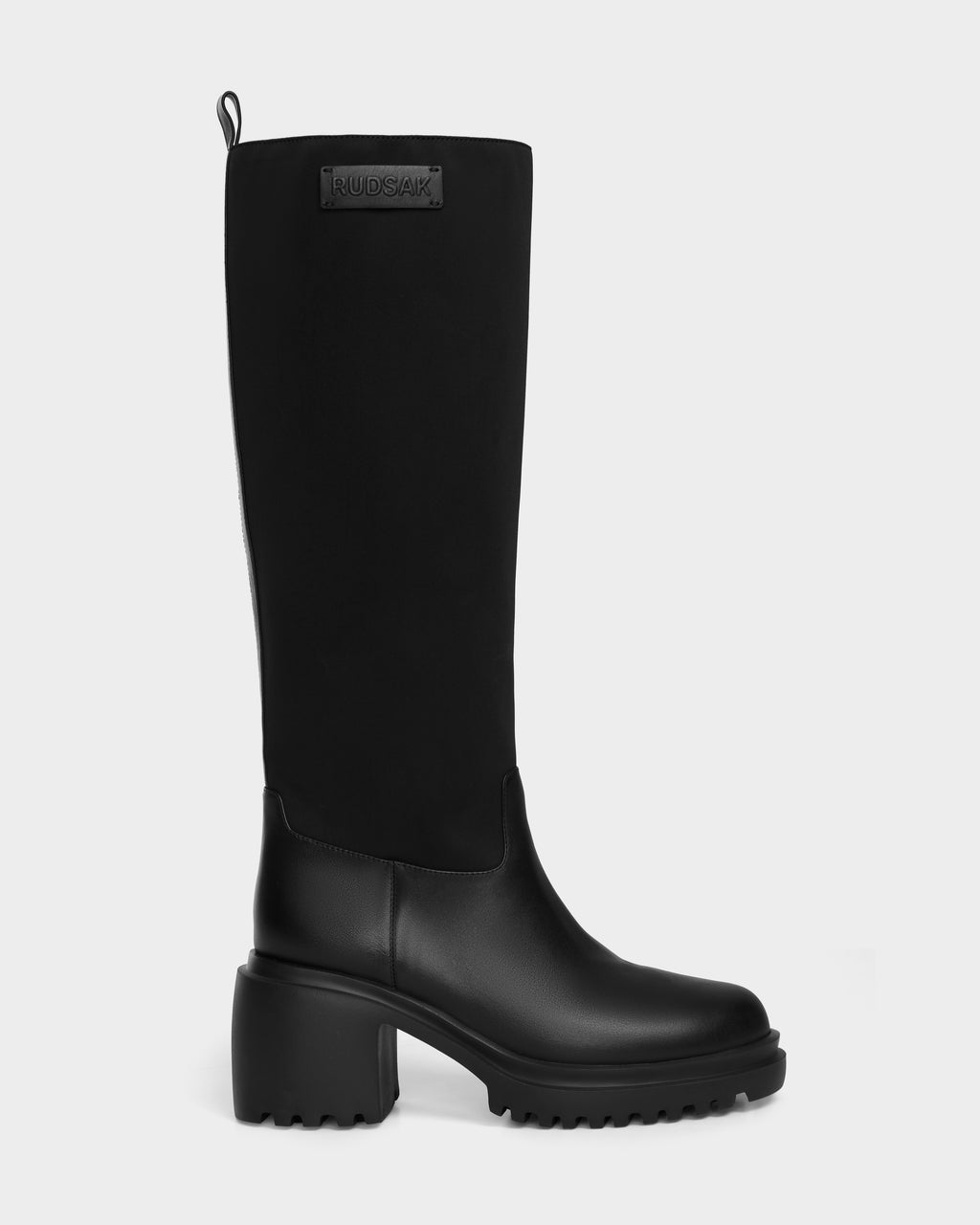 The TIARA - 8224529 Black by Rudsak is a black knee-high boot with a chunky heel, ridged sole, leather lower section, fabric upper, and a RUDSAK label near the top—an elevated take on women’s mid-heel boots.
