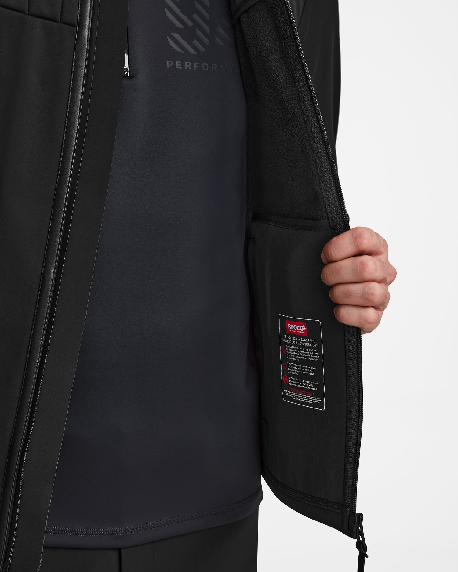 A person shows the inner pocket and care label of the Rudsak TREVOR - 6124519 Black mens ski jacket against a plain, light background, highlighting its technical features. They wear a dark shirt underneath.