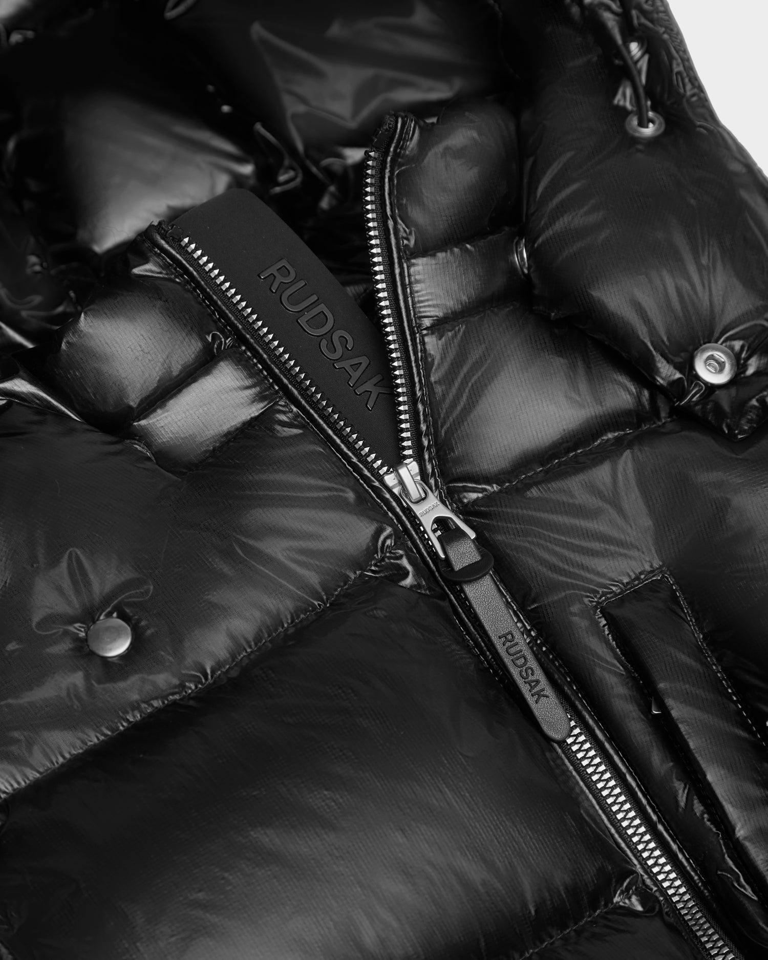 Close-up of the VINCE KS - 0124502 Black unisex winter jacket by Rudsak, featuring a glossy black finish, snap buttons, a silver zipper with Rudsak branding, and premium RDS-certified down insulation.